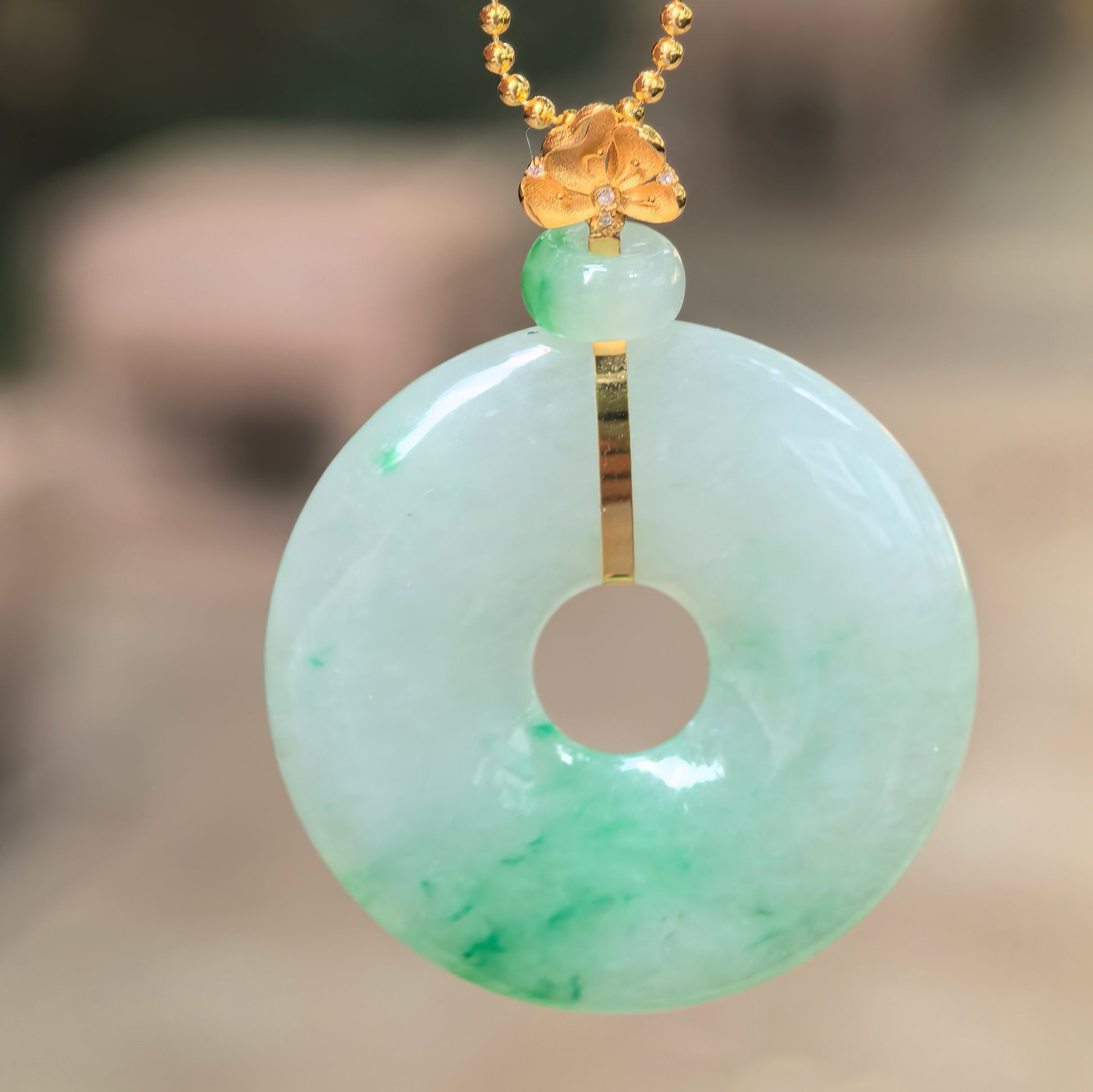 Natural Grade-A icy glutinous floating green jadeite donut pendant with an 18K gold floral bail hanging in natural light.