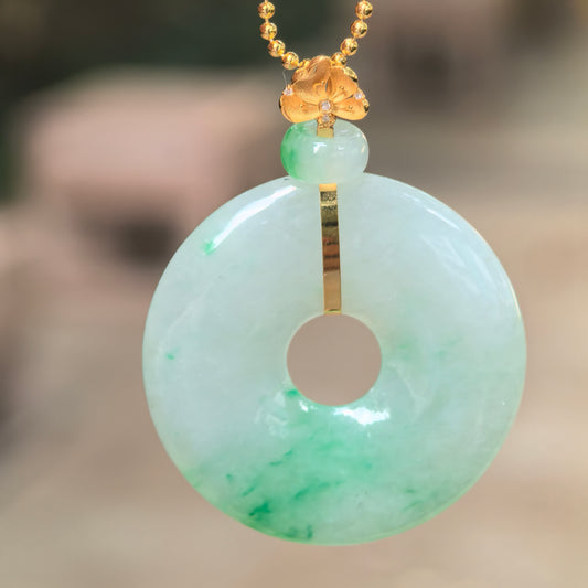Natural Grade-A icy glutinous floating green jadeite donut pendant with an 18K gold floral bail hanging in natural light.