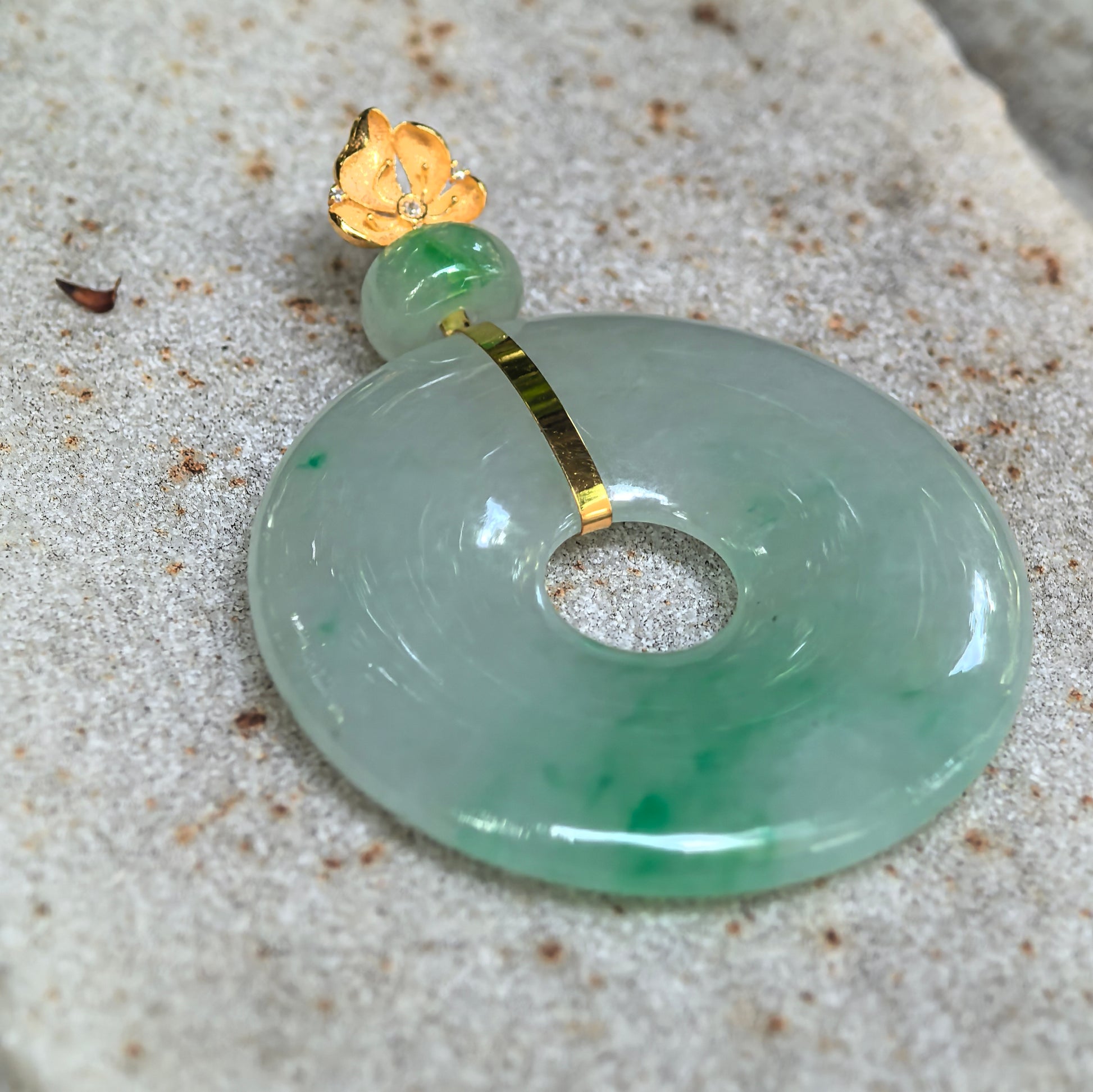 Close-up of the icy glutinous floating green jadeite donut pendant showing its polished surface, jadeite bead, and gold floral bail.