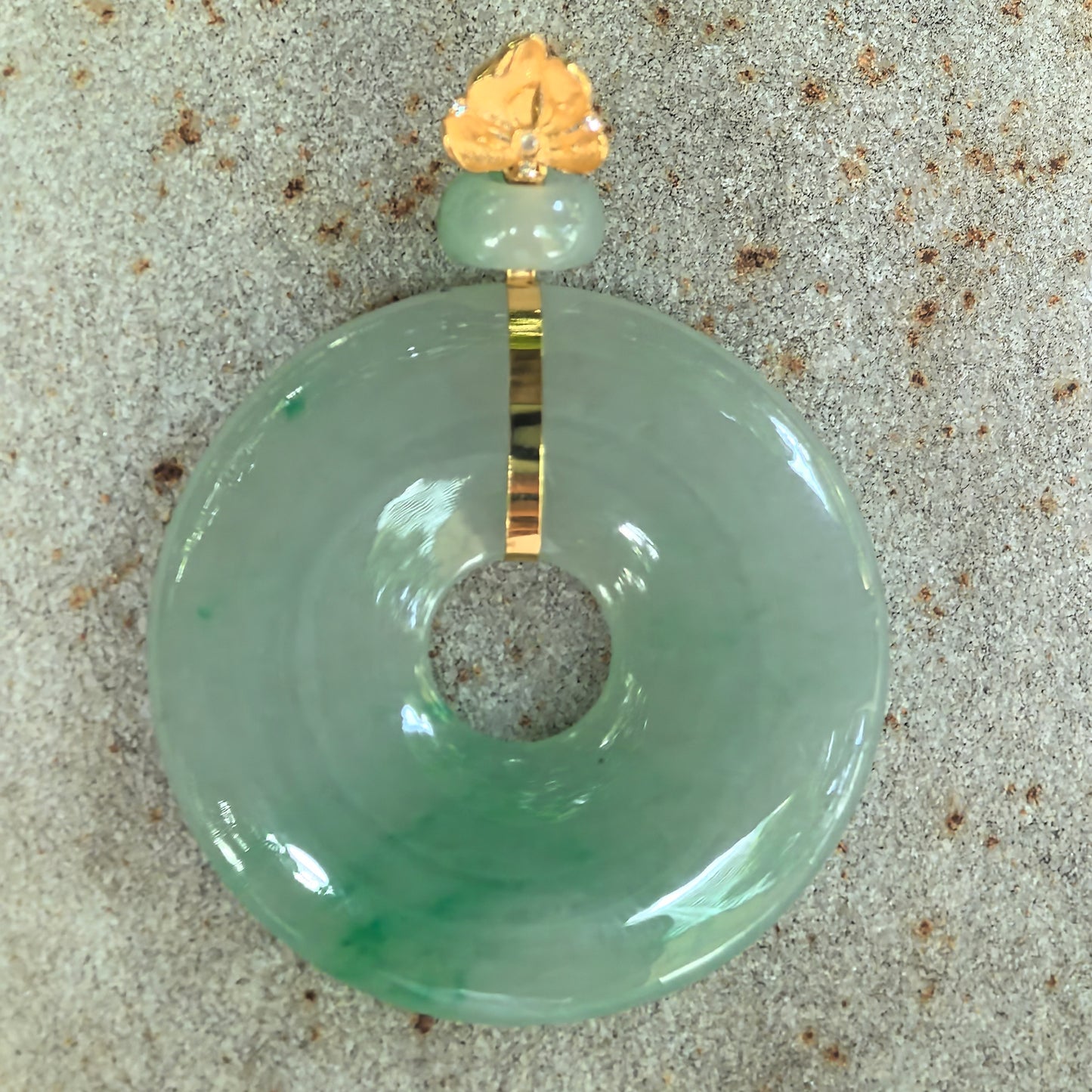 Natural Grade-A light green jadeite donut pendant with vivid floating green patterns displayed on a stone surface.