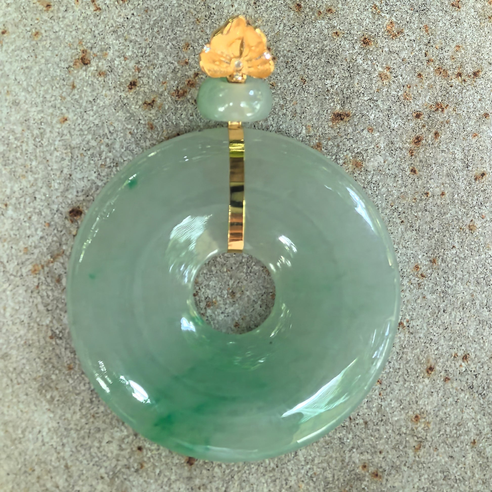Natural Grade-A light green jadeite donut pendant with vivid floating green patterns displayed on a stone surface.