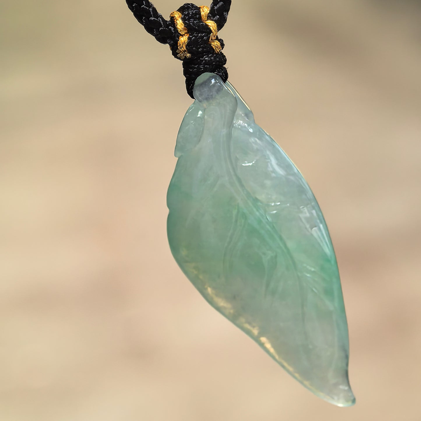 Natural Grade-A icy glutinous light green leaf jadeite pendant hanging from its black woven cord.