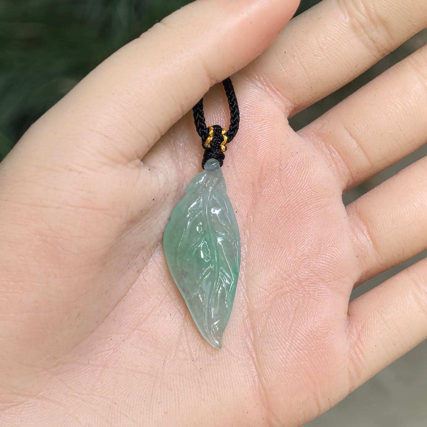 Light green Burmese jadeite leaf pendant displayed in the hand to show its elongated shape and compact proportions.