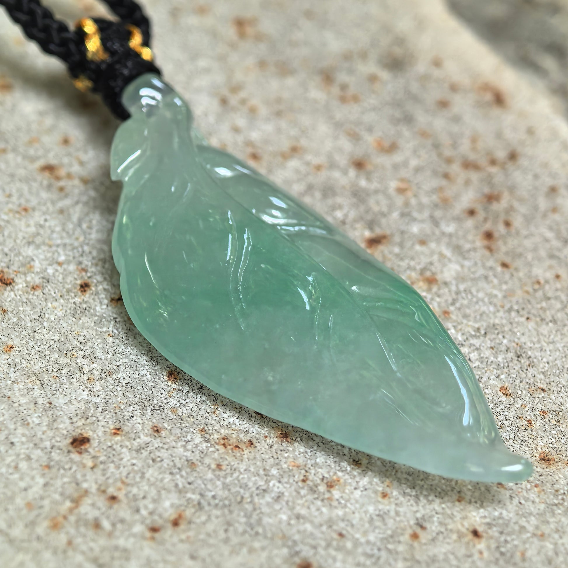 Angled close-up of the icy glutinous jadeite pendant showing its sweet green color, smooth luster, and leaf-vein carving.