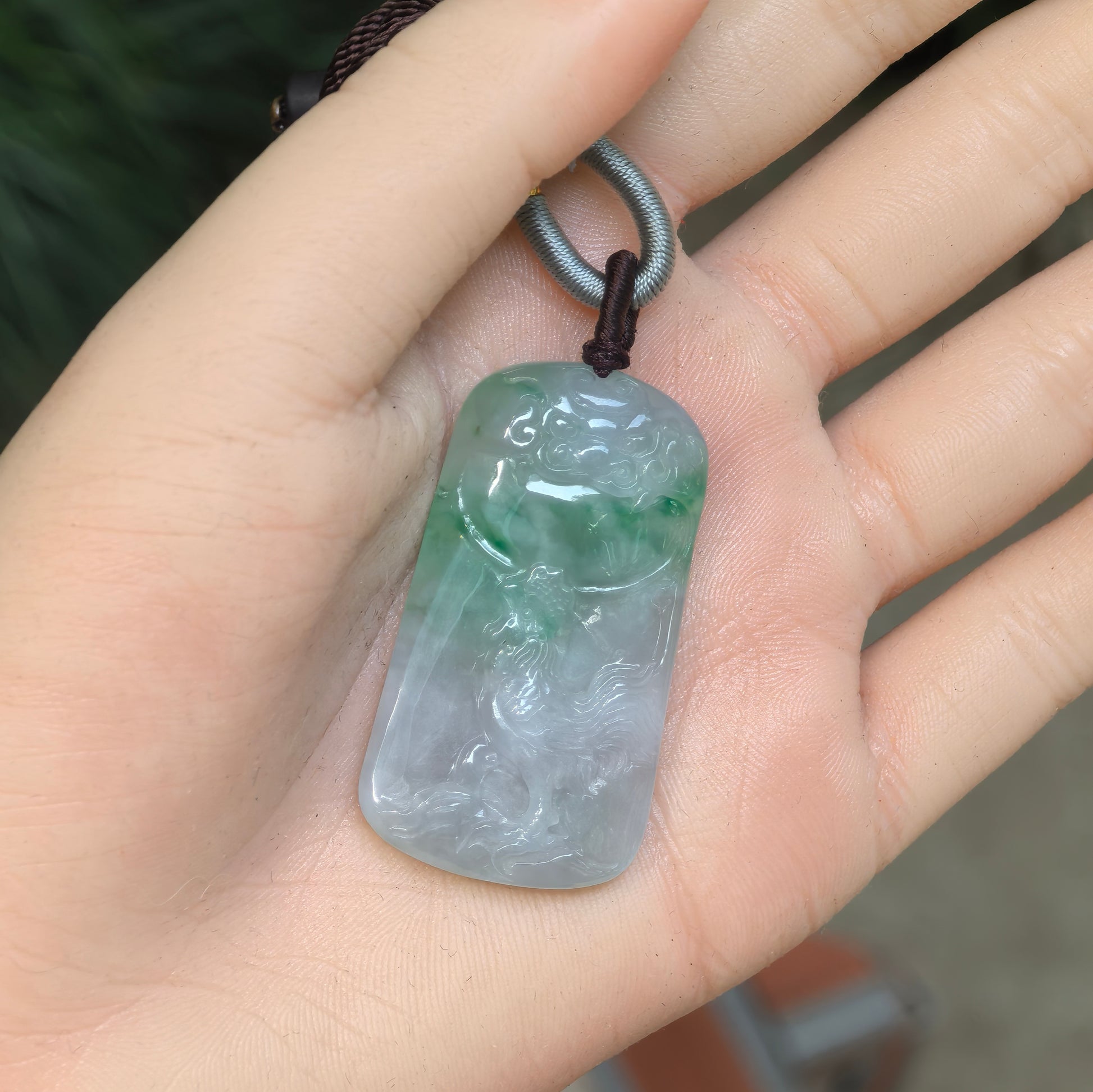 White-base green Burmese jadeite rooster pendant displayed in the hand to show its rectangular plaque shape and proportions.