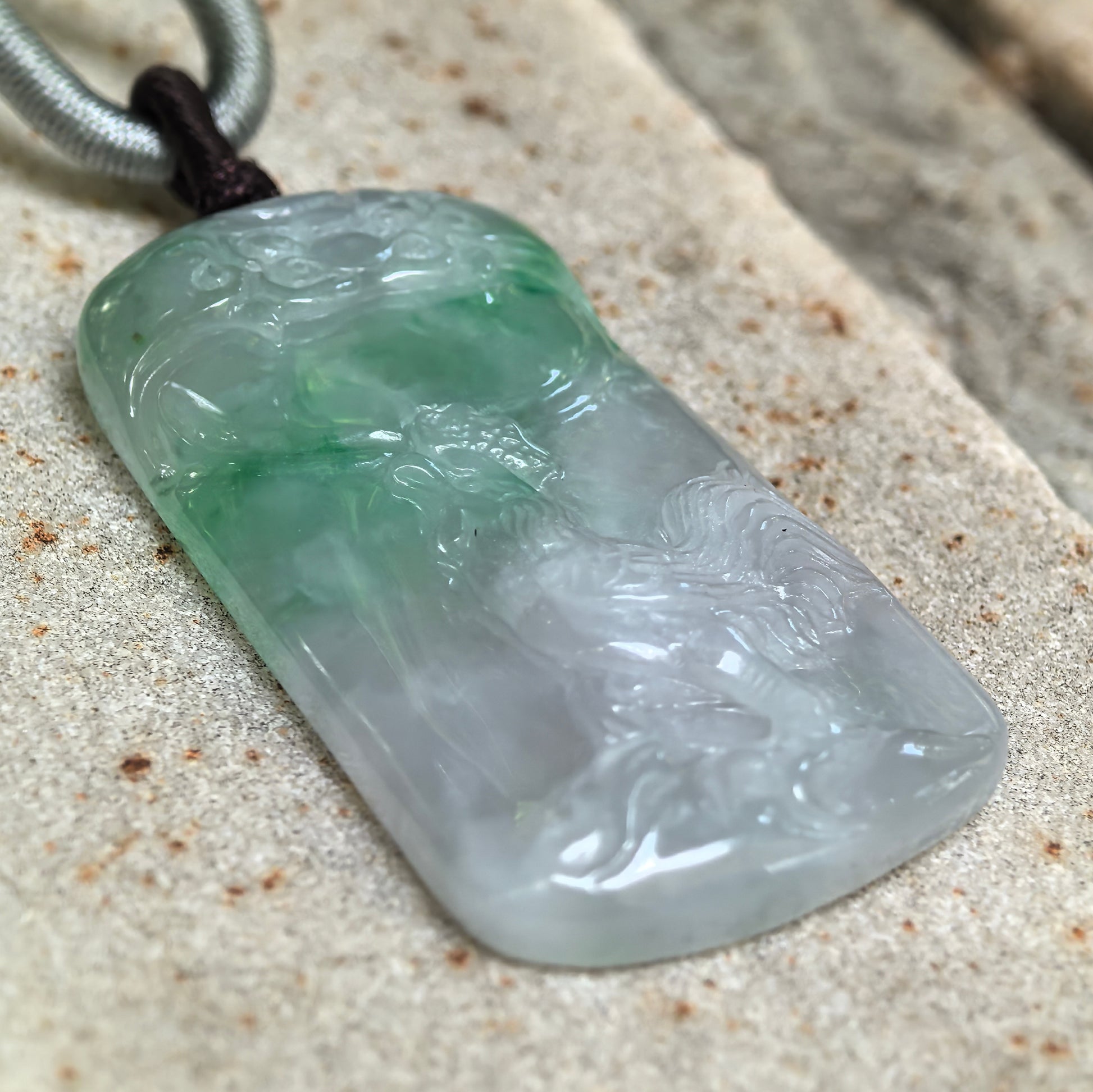 Angled close-up of the glutinous jadeite pendant showing green color distribution, smooth luster, and raised rooster carving.