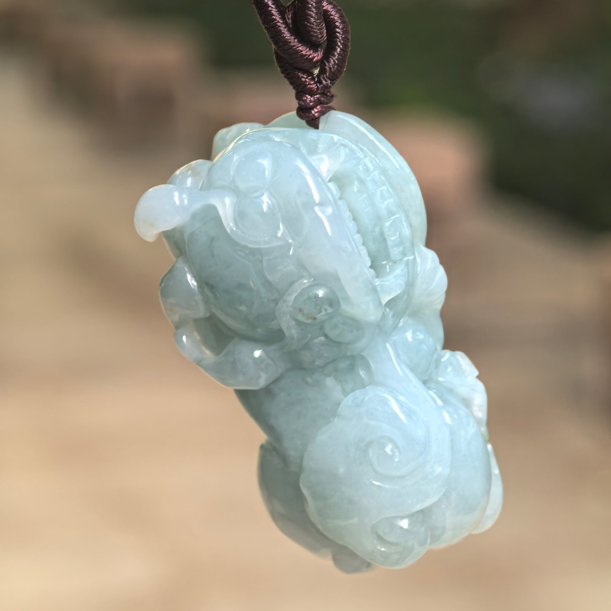 Natural Grade-A glutinous blue-green Pixiu jadeite pendant hanging from its cord and showing its substantial three-dimensional carving.