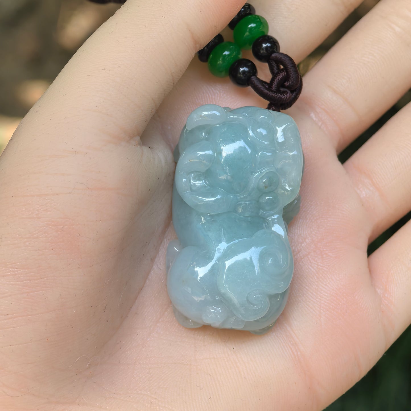 Hand-held blue-green Burmese jadeite Pixiu pendant showing its large size, thick profile, and polished surface.