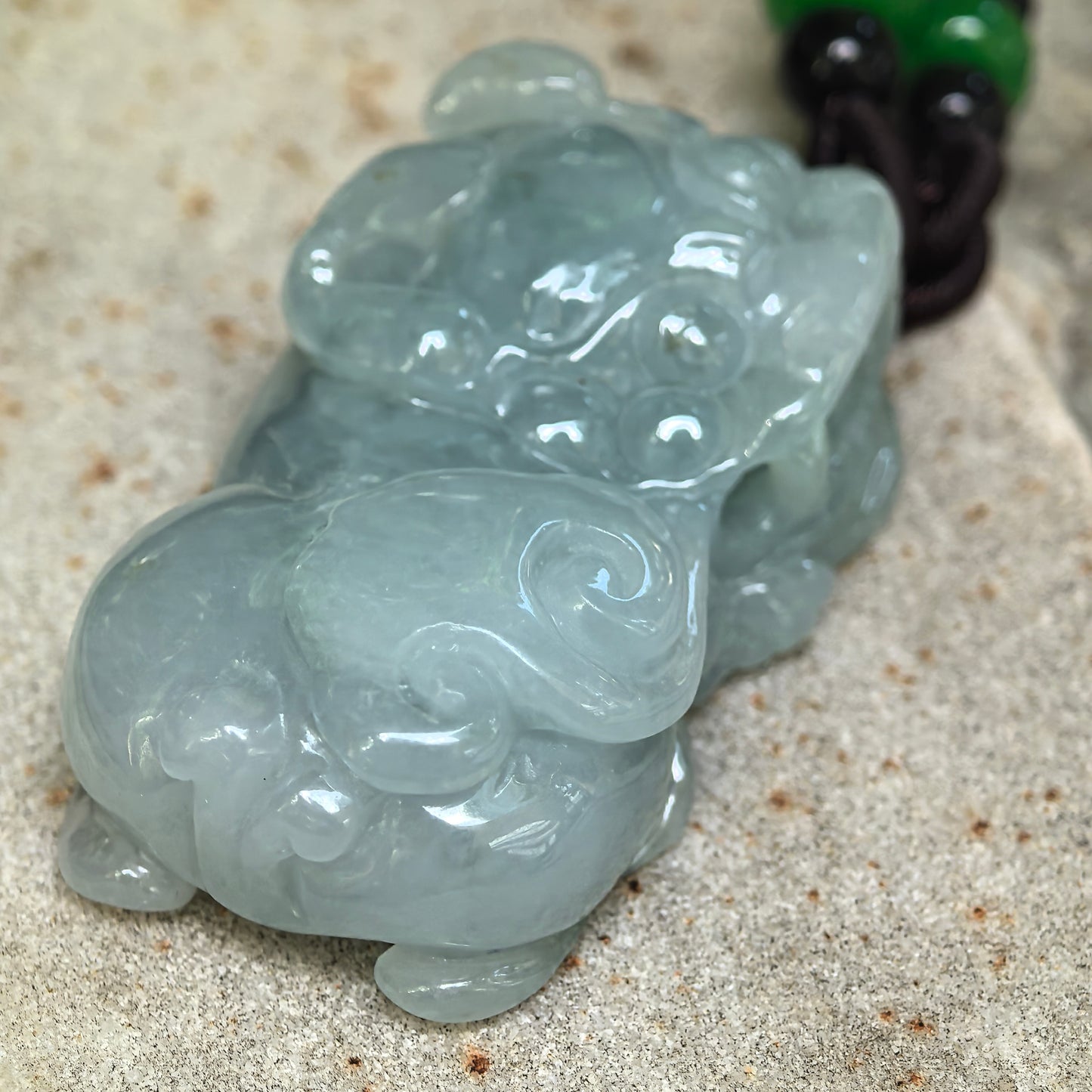 Close-up of the glutinous jadeite Pixiu pendant showing curled decorative details, rounded carving, and soft blue-green color.