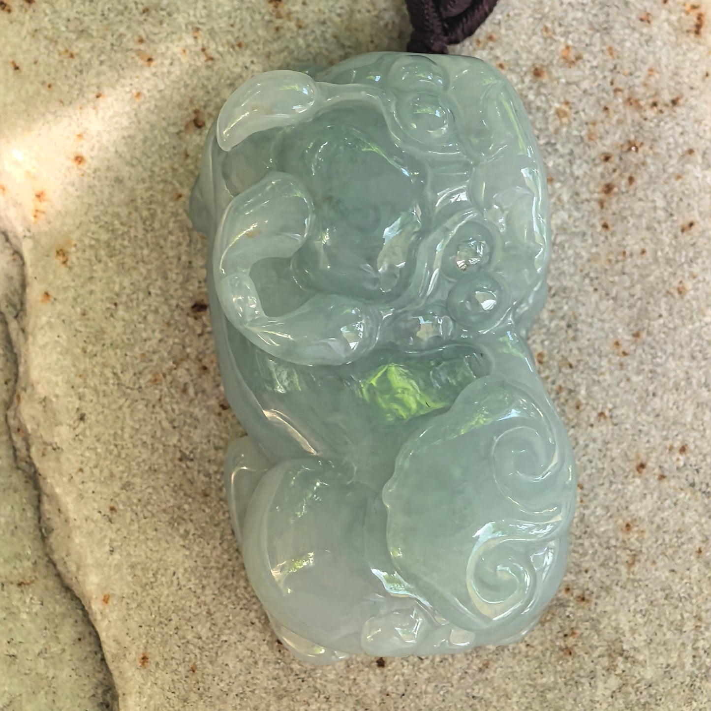 Detailed view of the large three-dimensional Pixiu jadeite pendant showing its open mouth, facial features, and cloud-like carving.