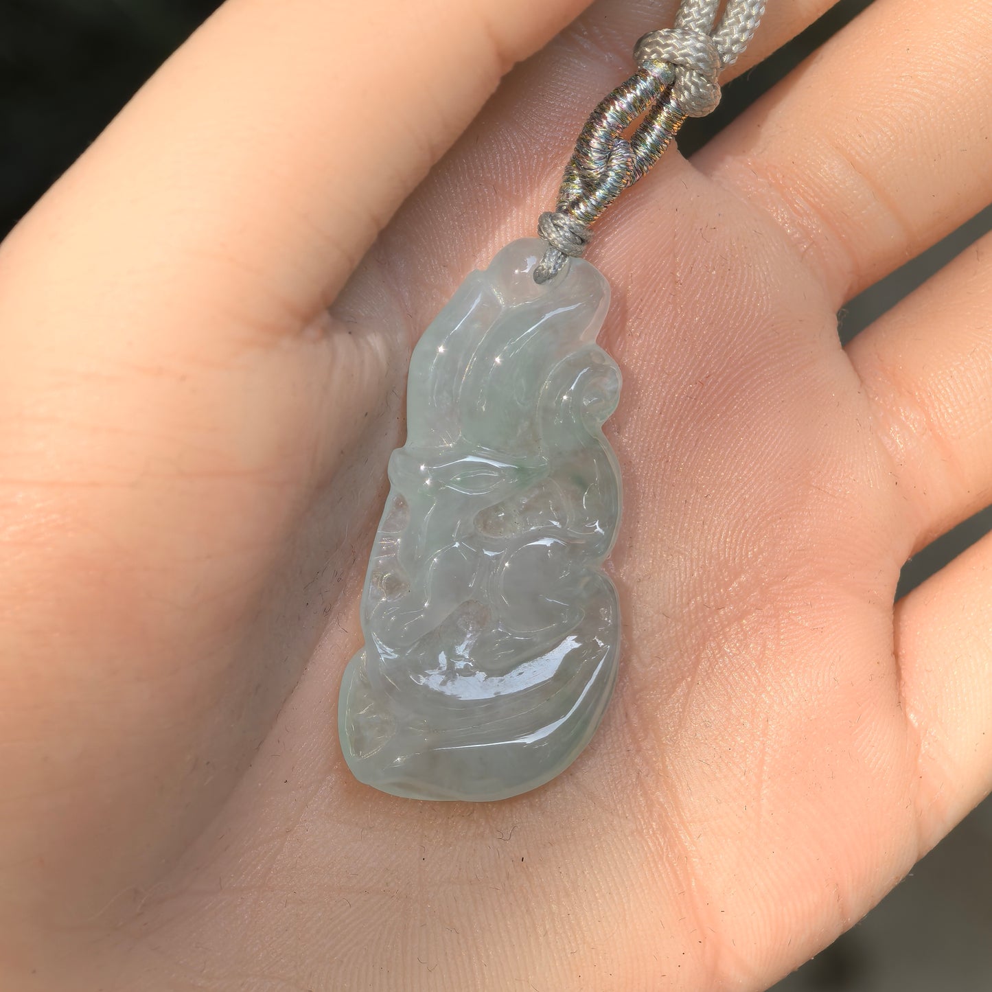 Hand-held light green jadeite fox pendant showing its elongated shape and carved details.