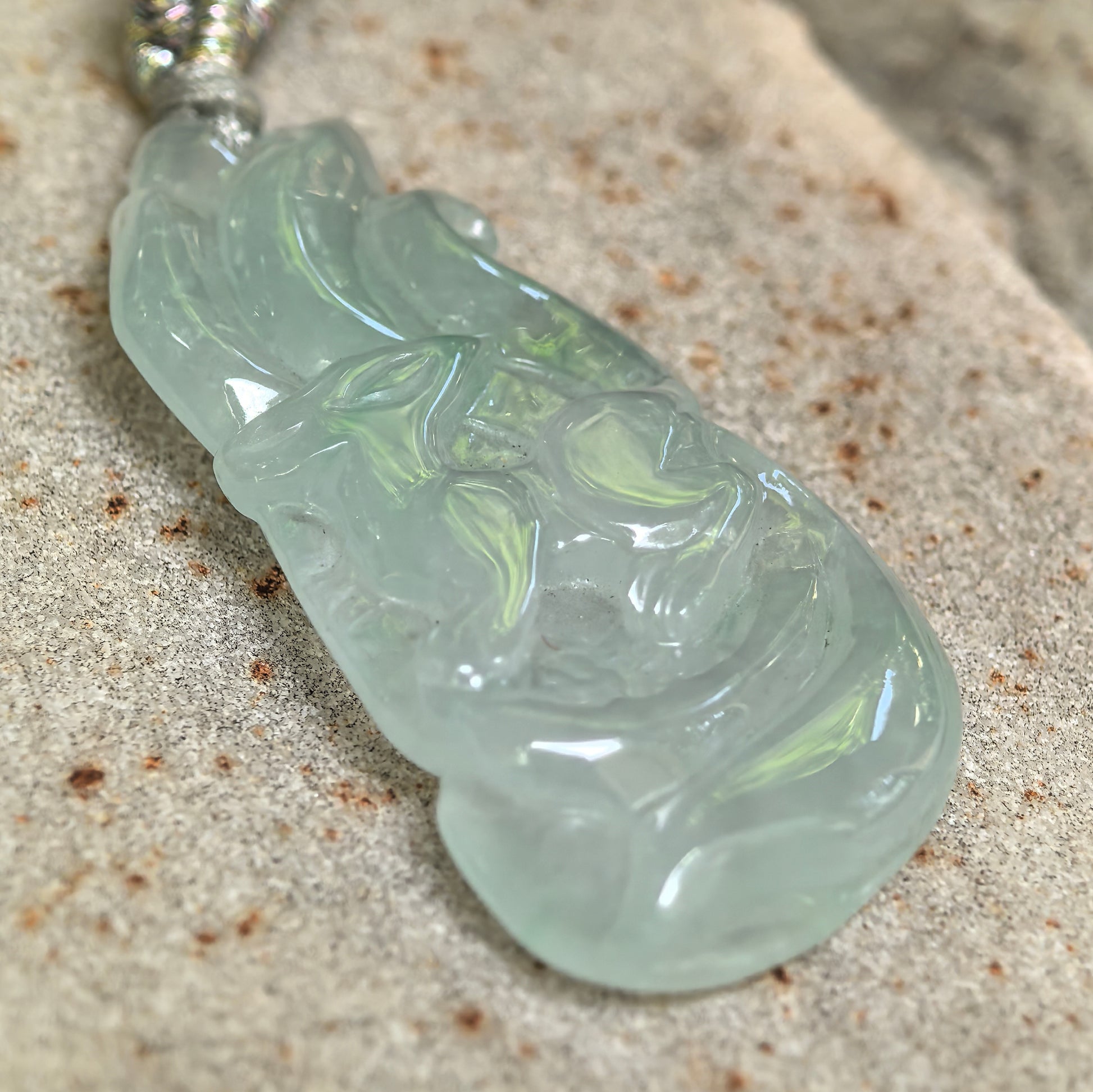 Close-up of an icy glutinous light green jadeite pendant with a three-dimensional nine-tailed fox carving.