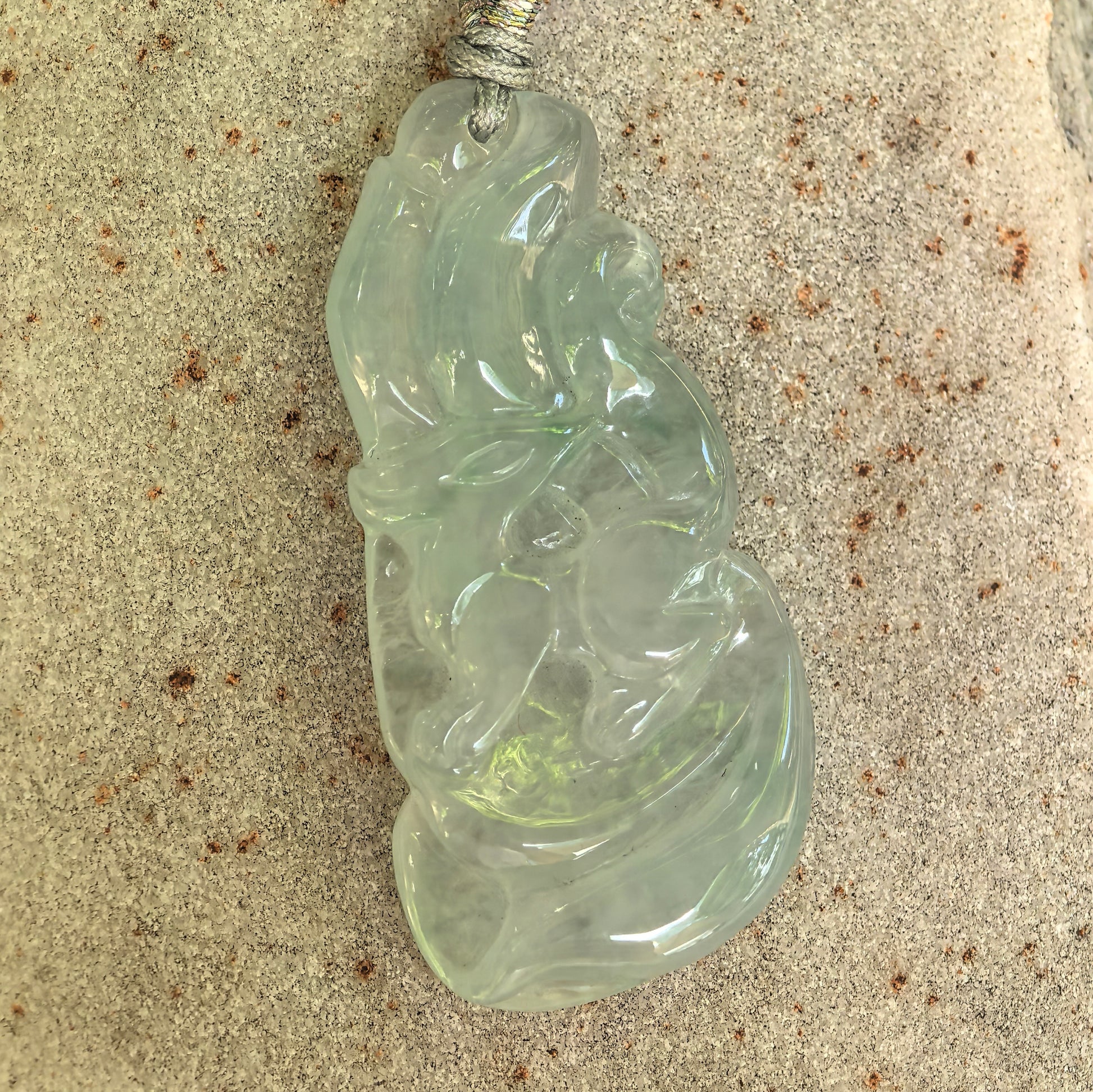Detailed front view of a natural light green nine-tailed fox jadeite pendant displayed on a stone surface.