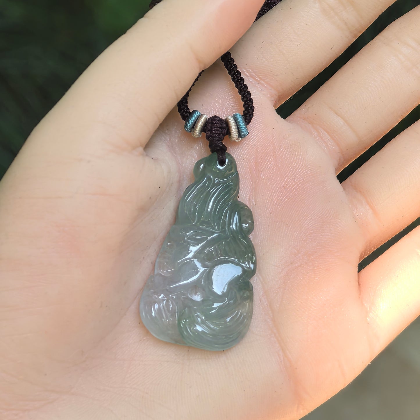 Hand-held blue-green Burmese jadeite pendant showing the elongated nine-tailed fox carving and translucent texture.
