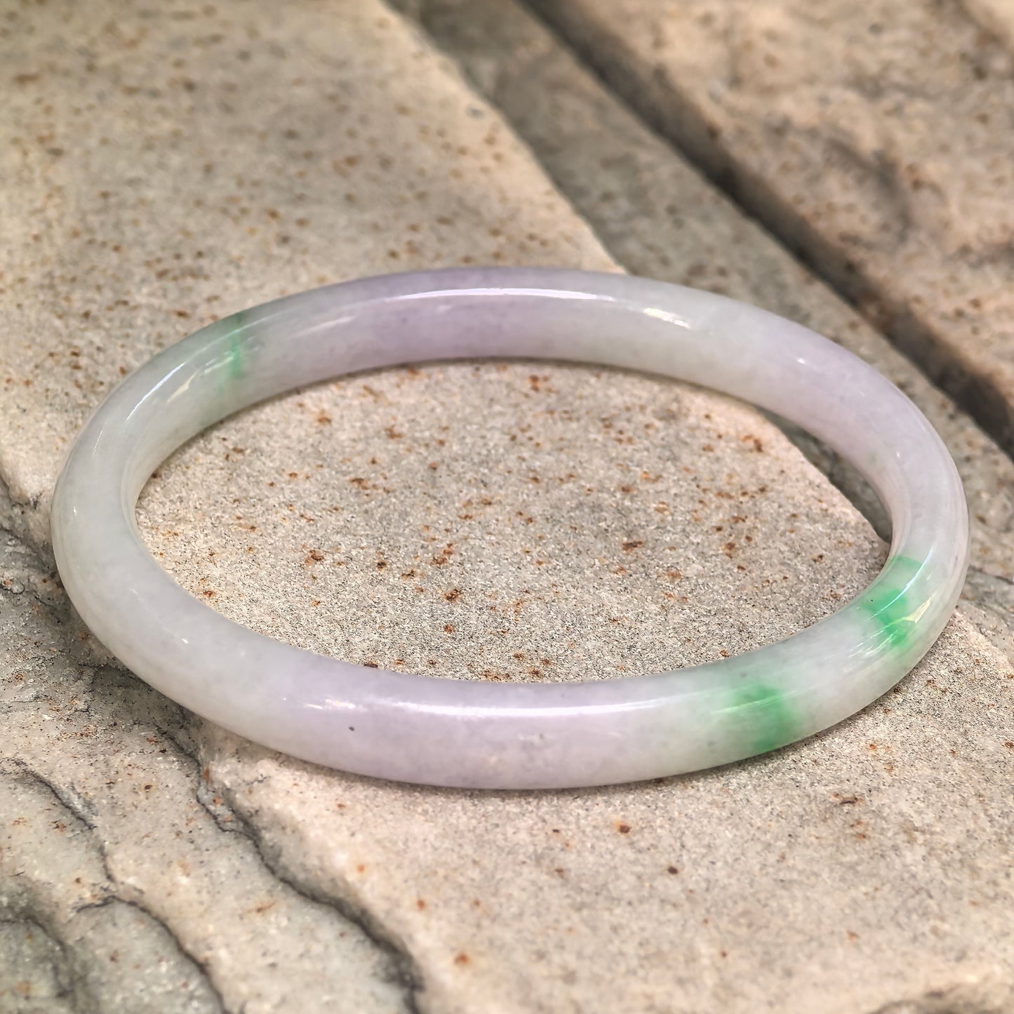 Close-up of the glutinous lavender-green oval jadeite bangle showing its polished surface and natural color distribution.