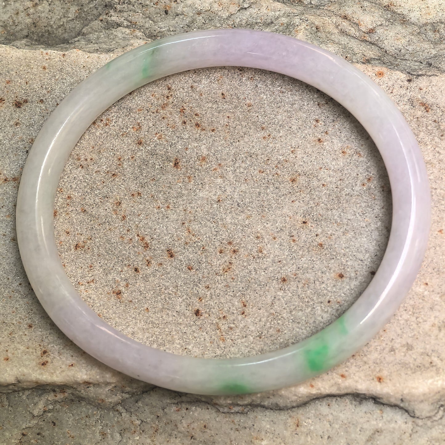 Full view of a slim oval Burmese jadeite bangle with pale lavender and localized green color.