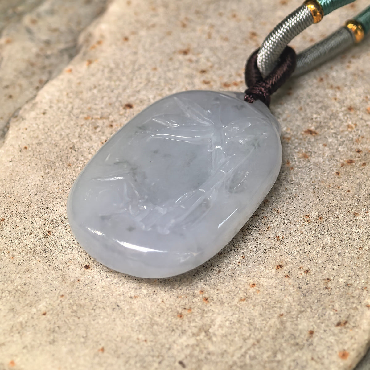 Angled close-up of the glutinous pale lavender jadeite pendant showing the polished surface and carved bamboo details.