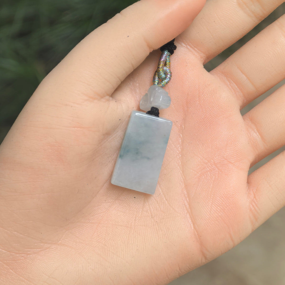 Hand-held view of the light green rectangular jadeite plaque pendant showing its compact proportions and cloud spacer.