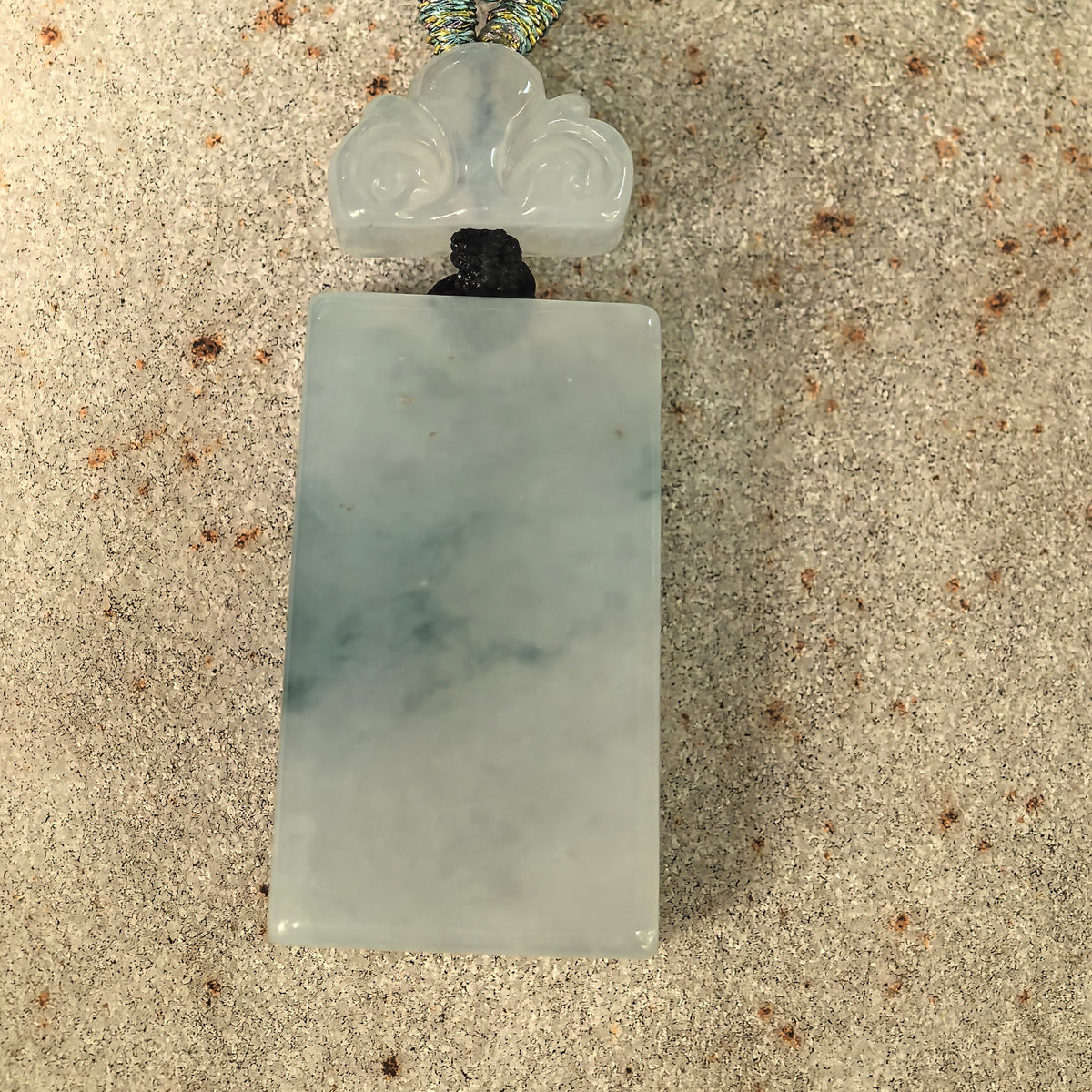 Front view of the light green plain plaque jadeite pendant with softly rounded edges and a carved cloud-shaped spacer.