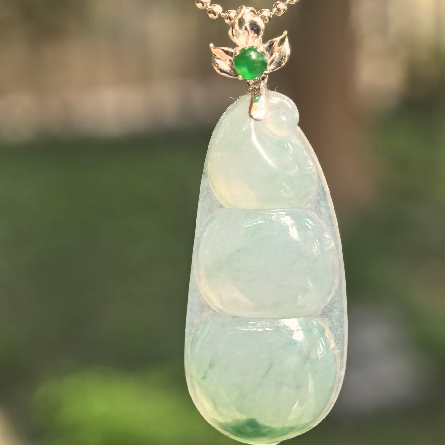 Natural Grade-A icy glutinous light green bean jadeite pendant hanging from an 18K gold floral bail.