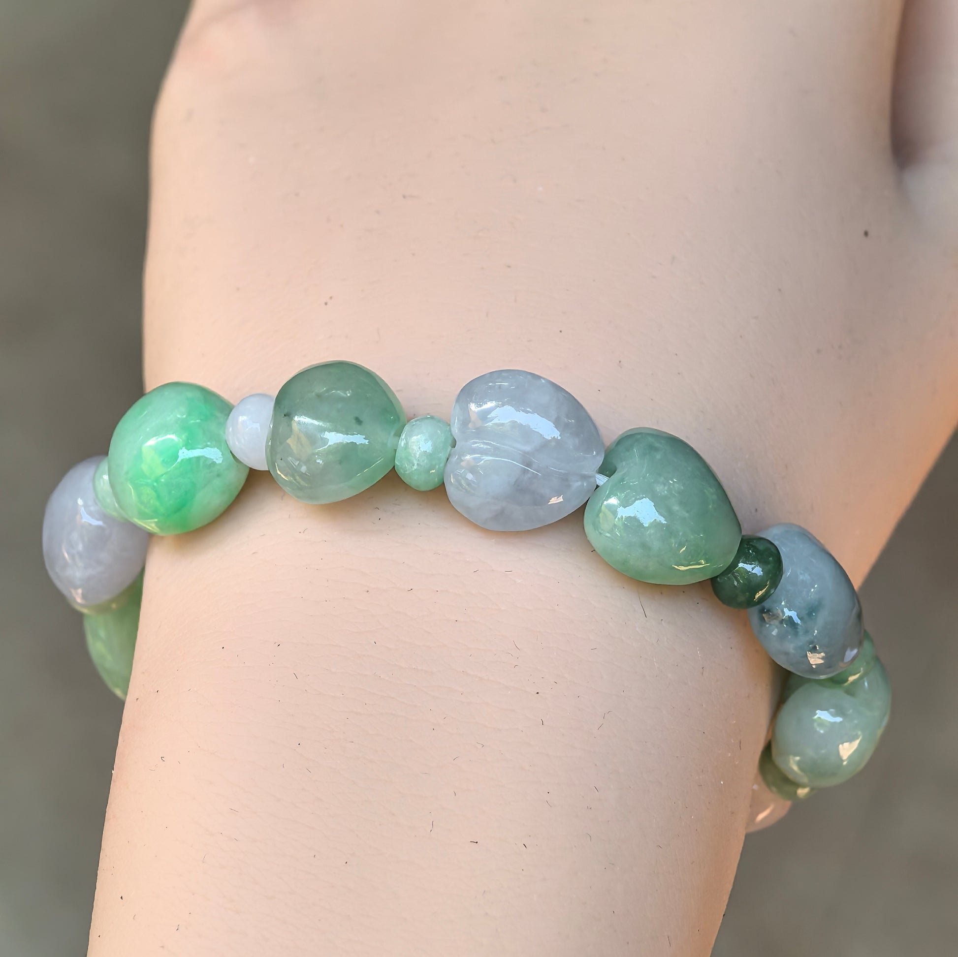 Close-up wearing view of a natural Grade-A glutinous green and pale lavender peach-shaped jadeite bracelet.