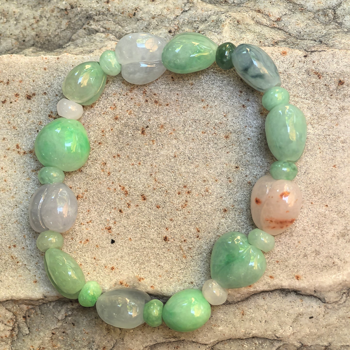 Full top-down view of the glutinous multicolor jadeite bracelet showing twelve larger carved beads and small spacers.