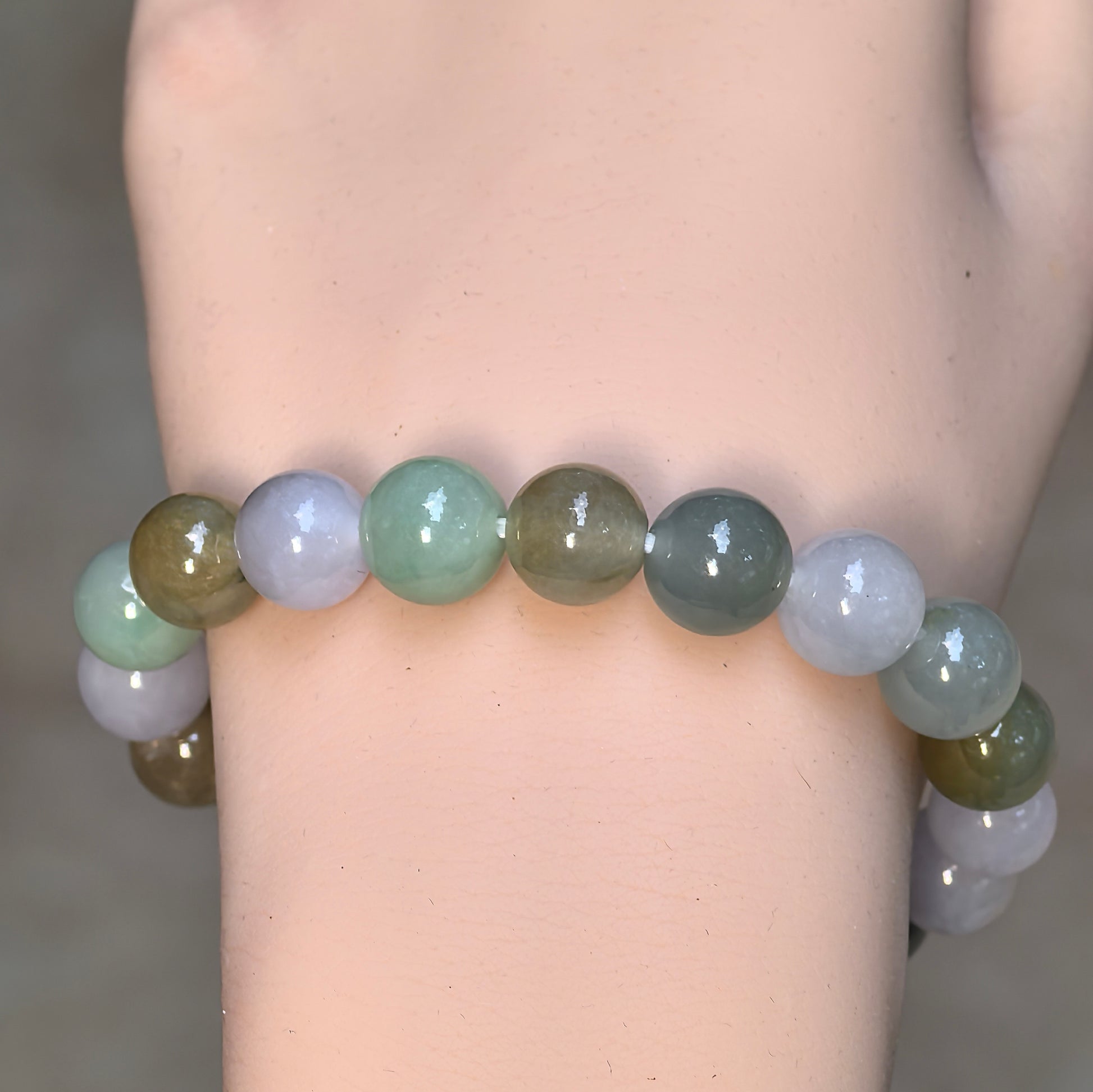 Front wrist view of the Burmese jadeite bracelet showing light green, white, gray-green, and yellow-brown beads.