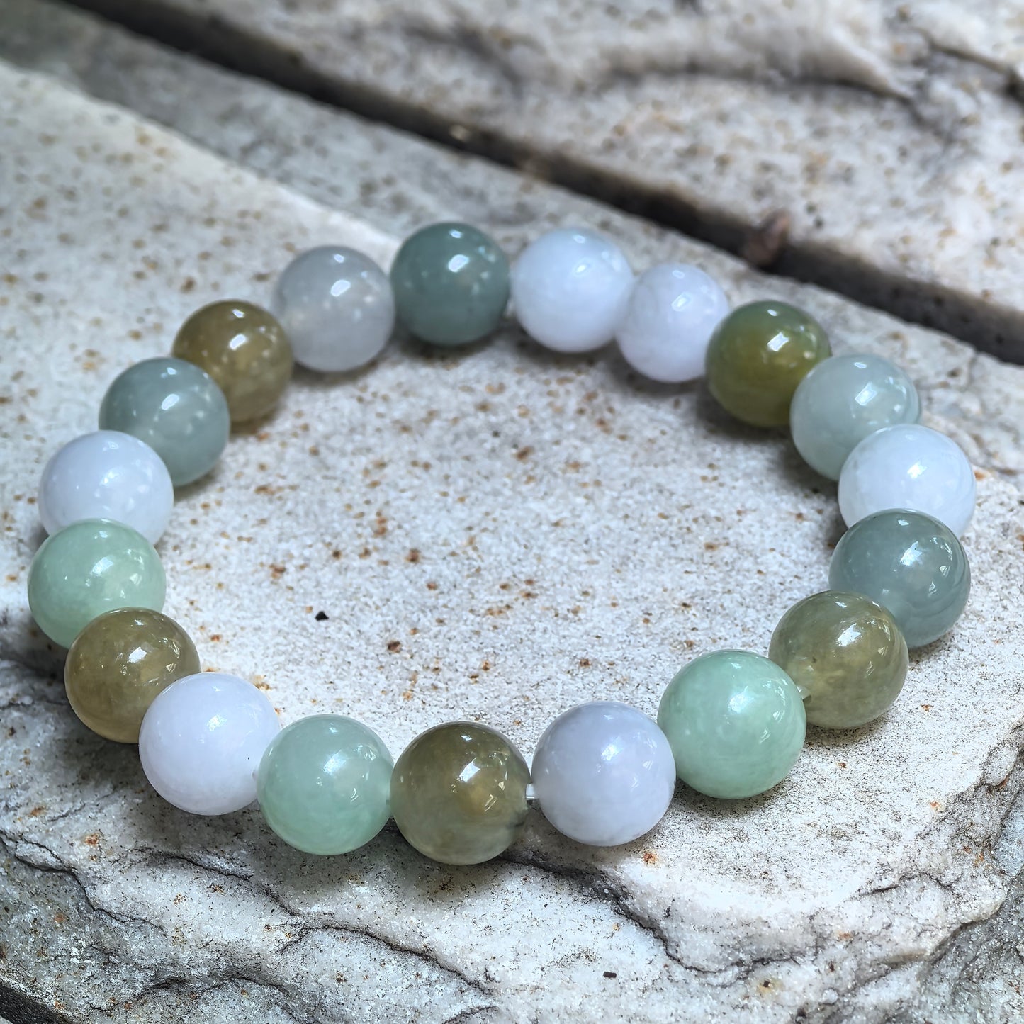 Natural Grade-A multicolor jadeite round-bead bracelet arranged on a textured stone surface.