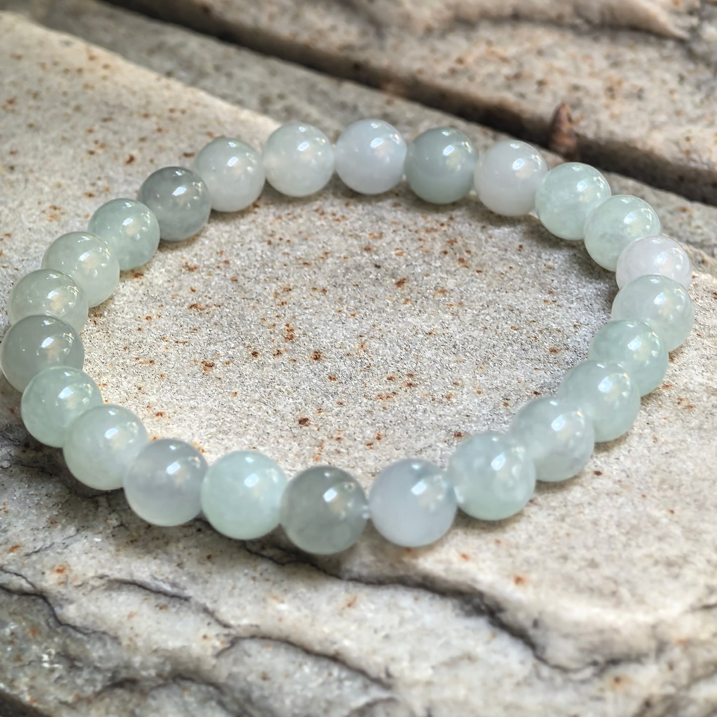 Natural Grade-A light green jadeite round-bead bracelet arranged on a textured stone surface.