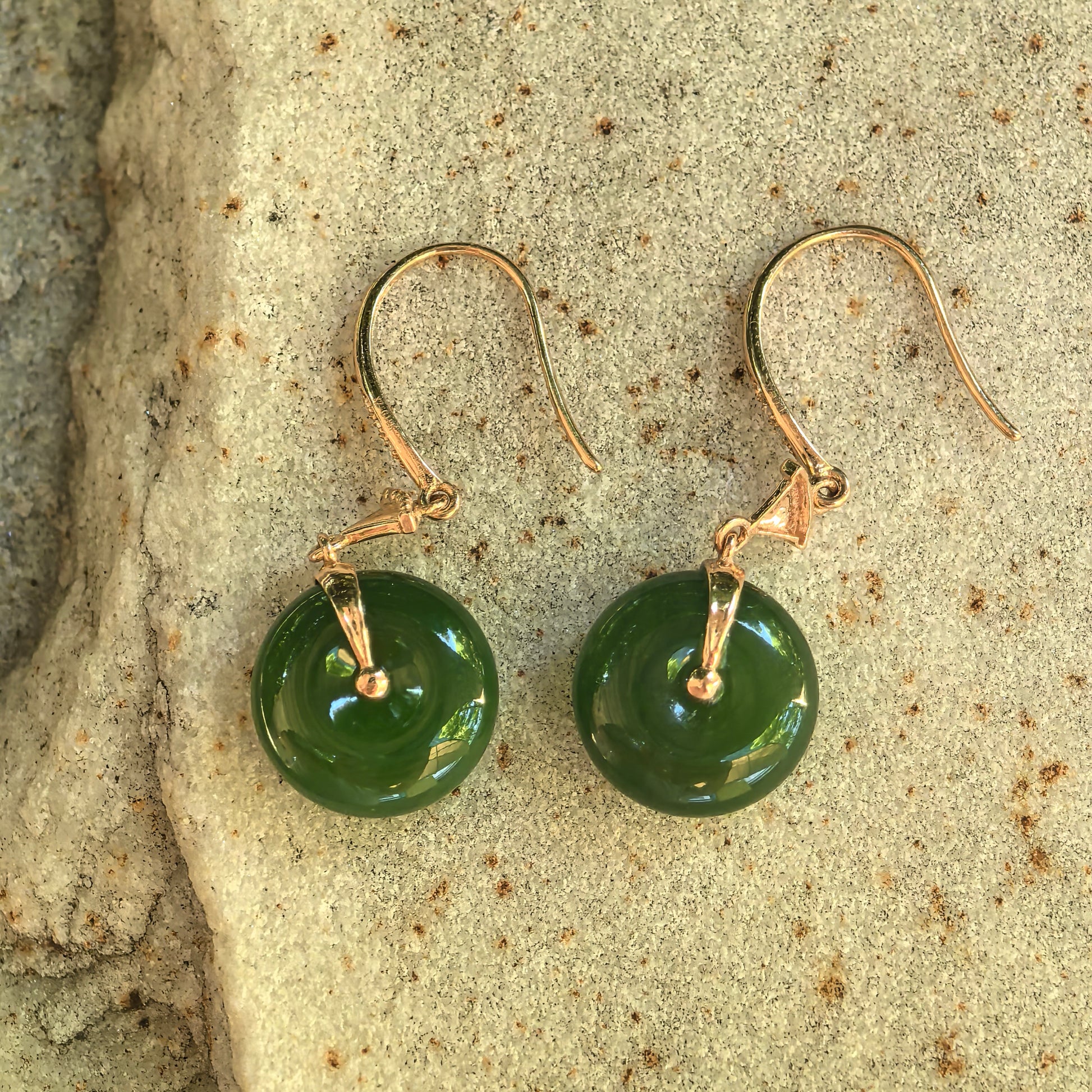 Top view of the natural green nephrite earrings showing the circular openings, smooth polish, and 18K gold settings.