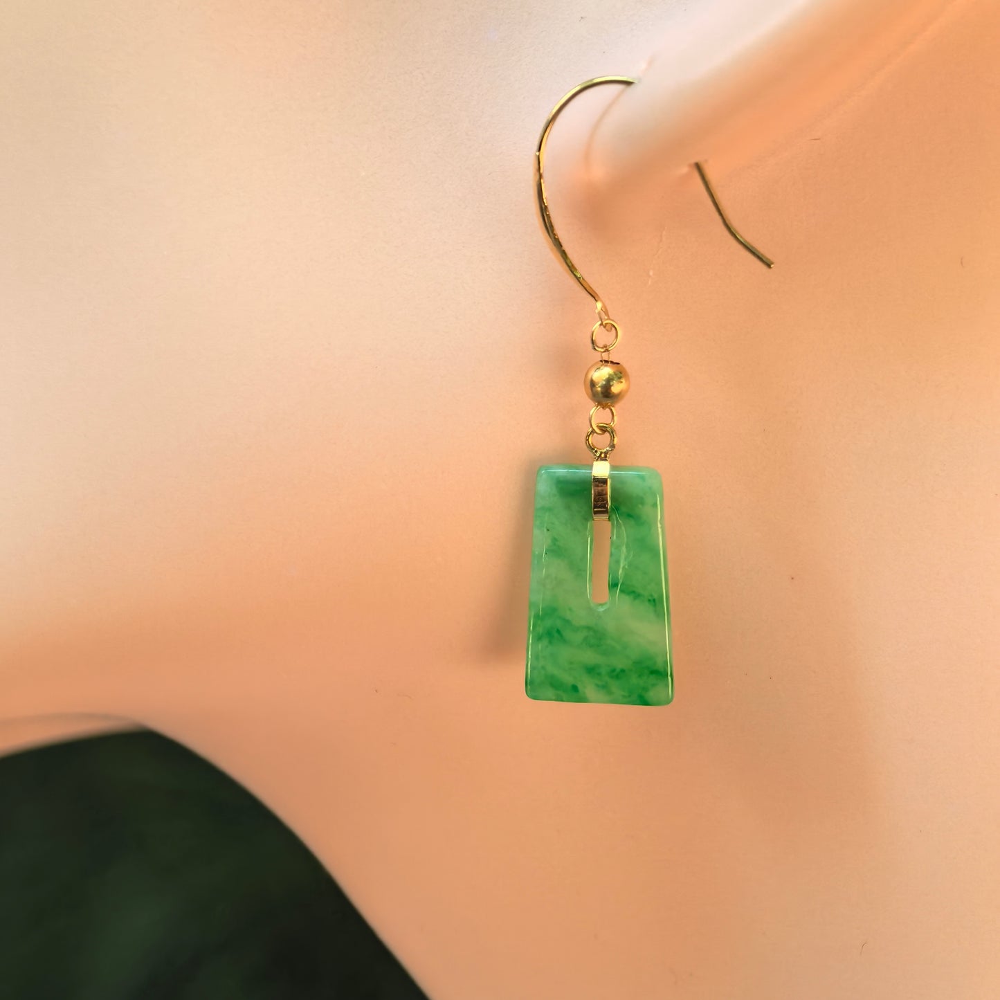 Natural Grade-A glutinous green rectangular jadeite drop earring with an 18K gold hook shown on an ear display.