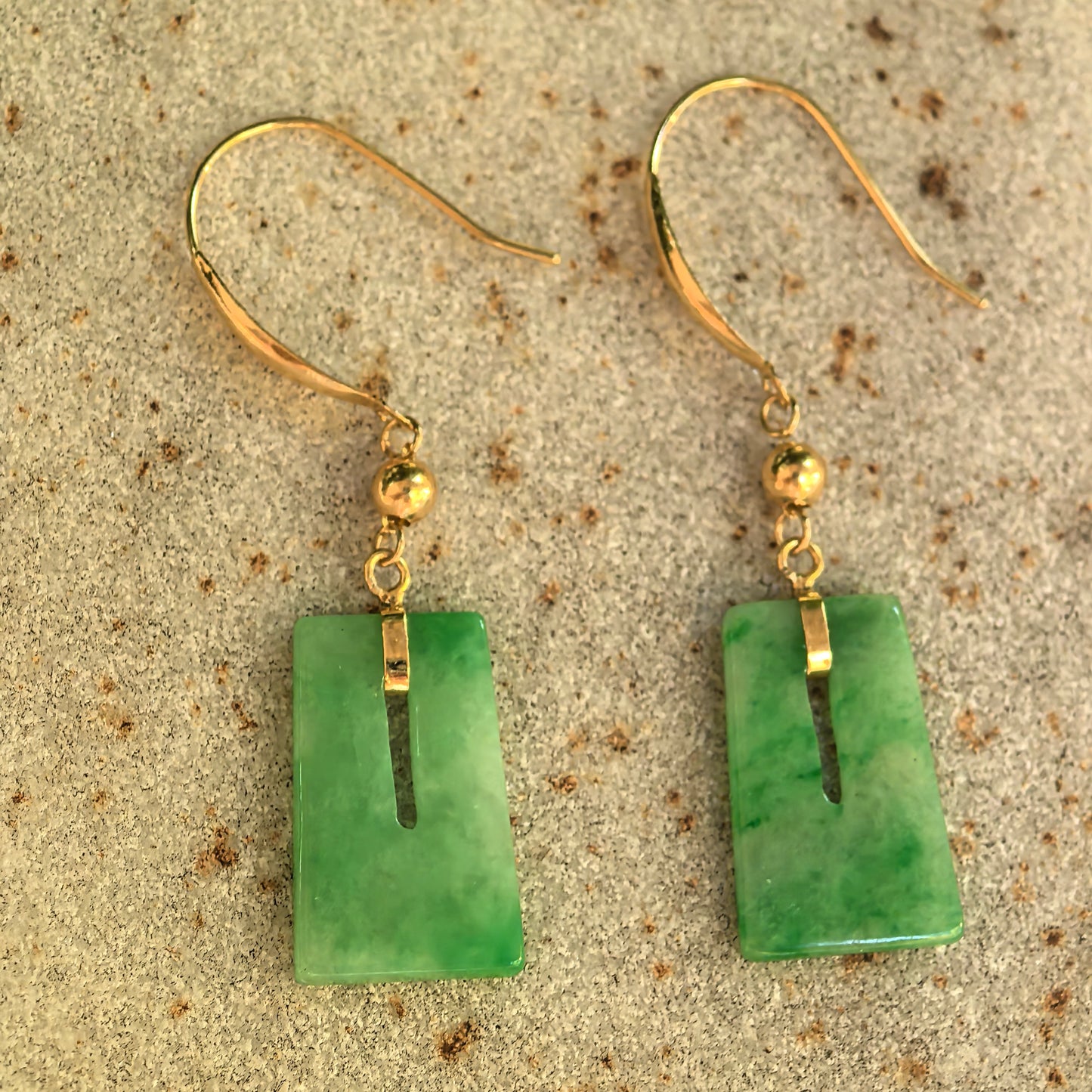 Front view of rectangular green jadeite drop earrings showing the elongated central openings and polished gold connectors.