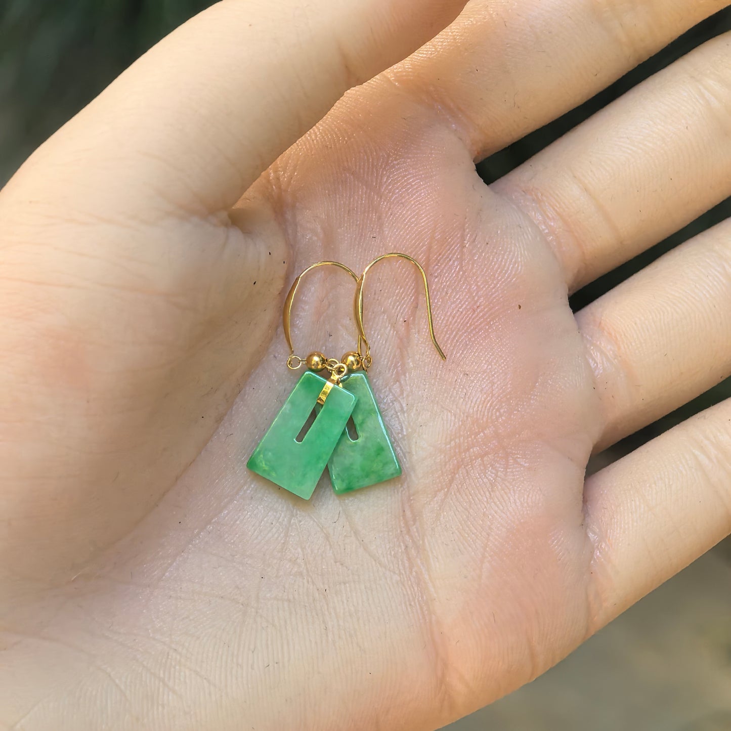 Hand-held view of the natural Grade-A green jadeite earrings showing their petite proportions and 18K gold fittings.