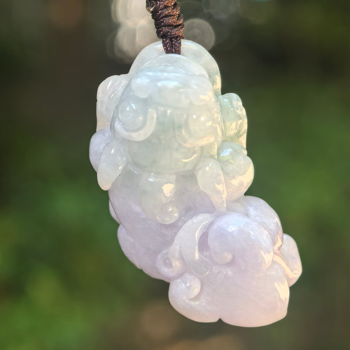 Natural Grade-A glutinous light green and pale lavender Pixiu jadeite pendant hanging from a dark woven cord.