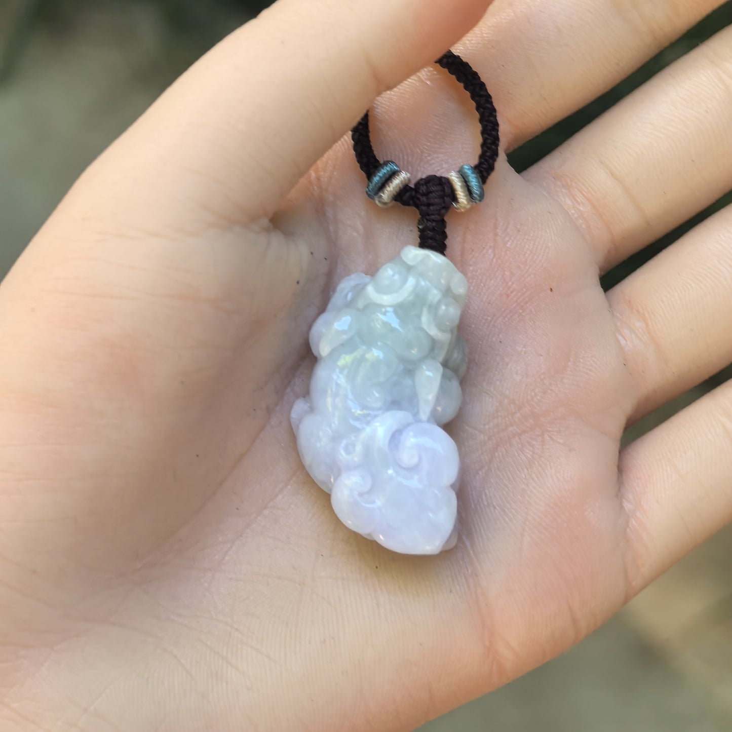Hand-held view of the three-dimensional spring color Pixiu jadeite pendant showing its compact proportions.