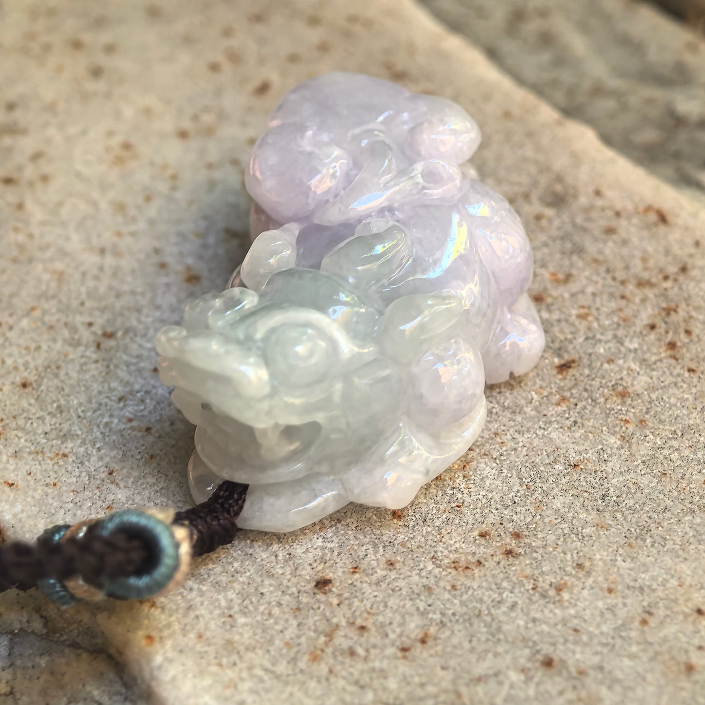 Close-up of the pale lavender and light green Pixiu jadeite pendant showing the rounded face and polished carving.