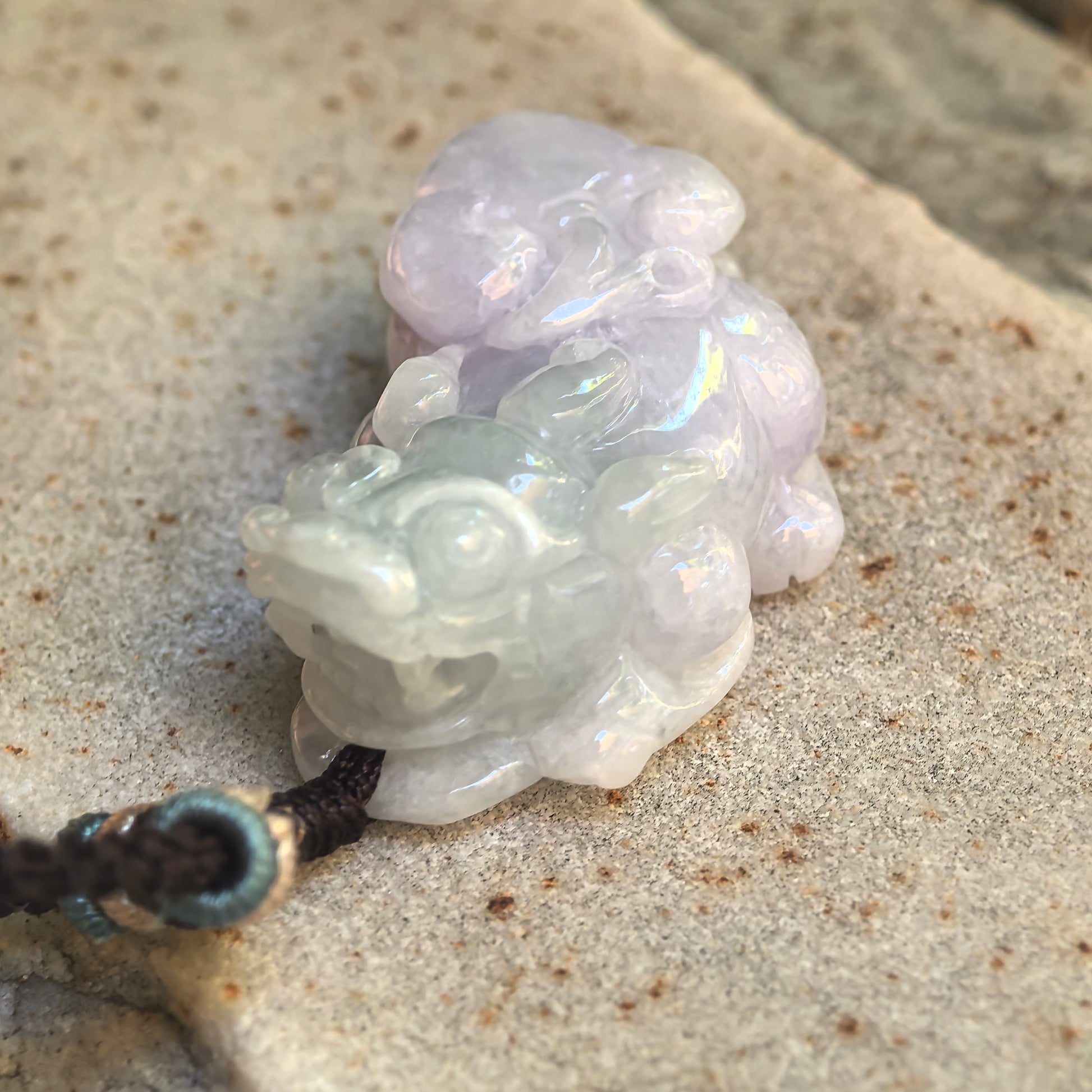 Close-up of the pale lavender and light green Pixiu jadeite pendant showing the rounded face and polished carving.
