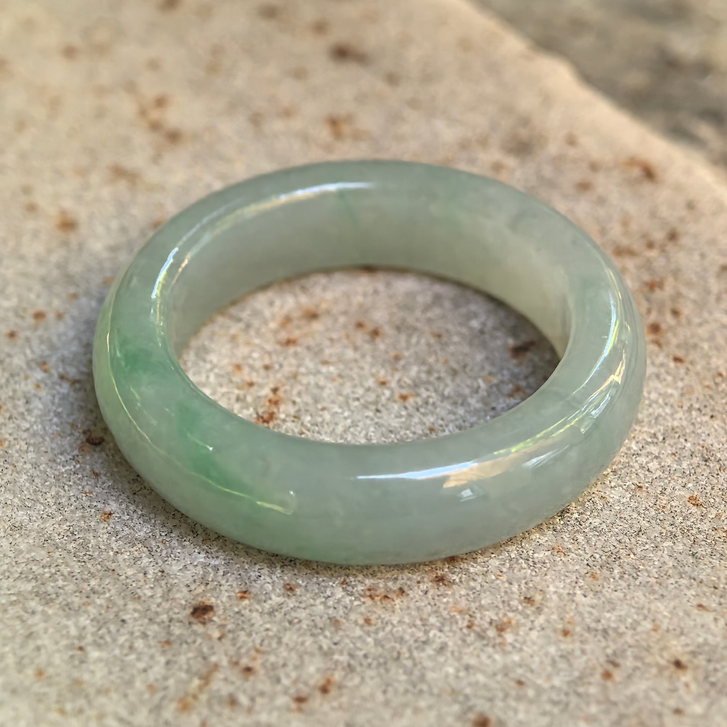 Natural light green jadeite ring band displayed upright on a textured stone surface.