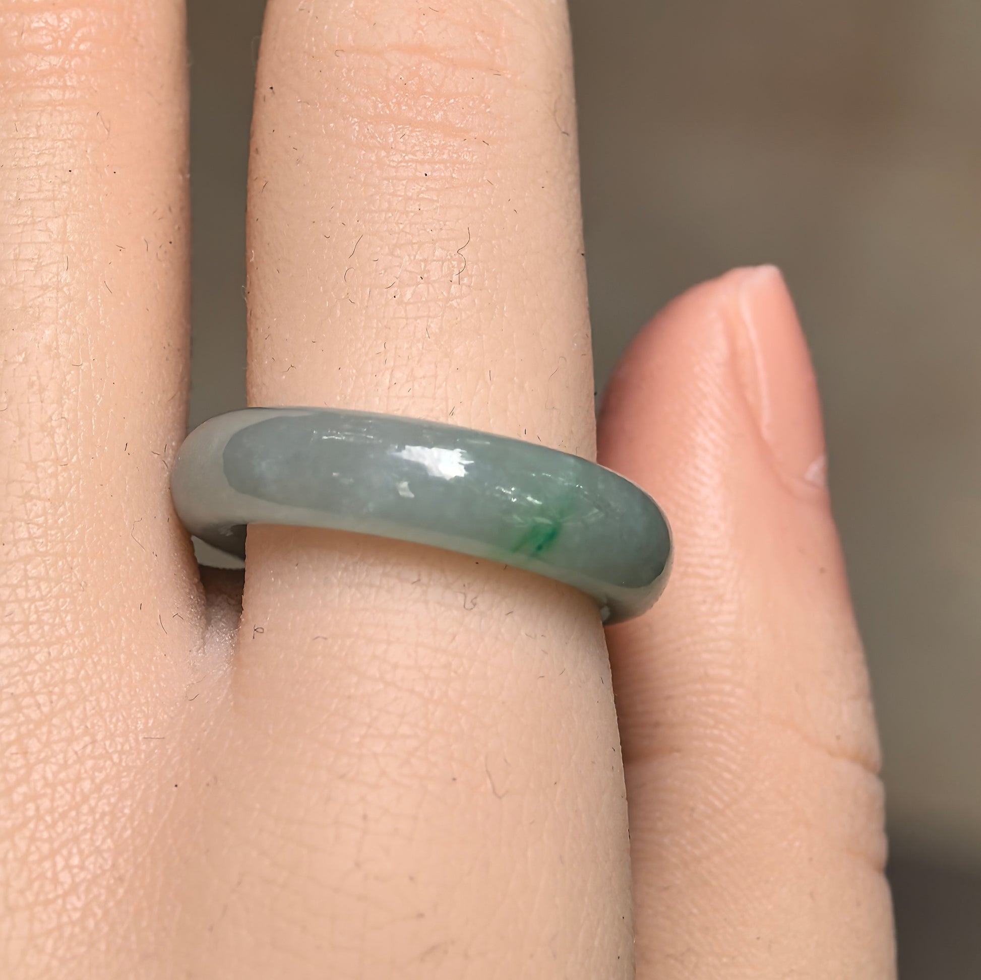 Close-up wearing view of a light green Burmese jadeite ring band with a small concentrated green accent.