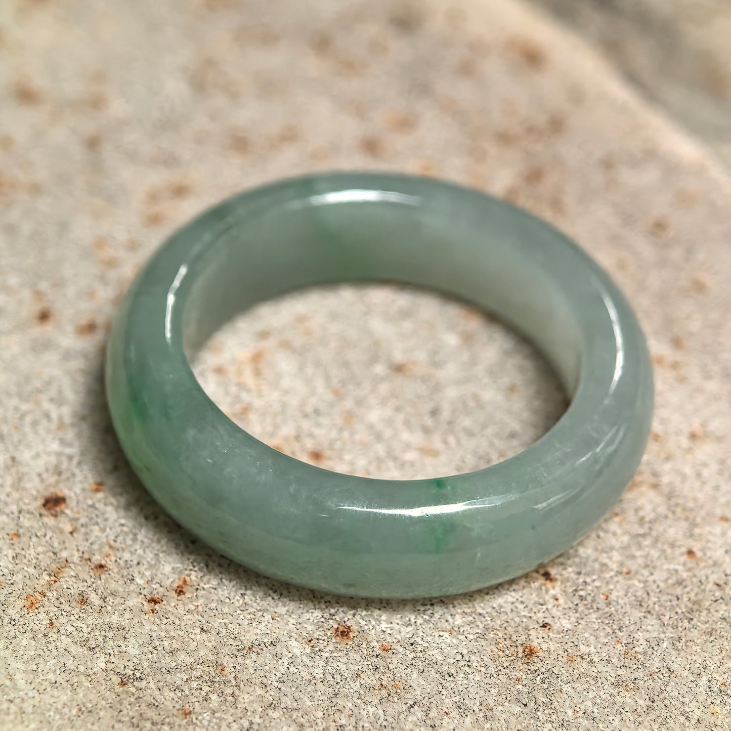 Natural light green jadeite ring band displayed on a stone surface, showing its translucent icy glutinous texture.