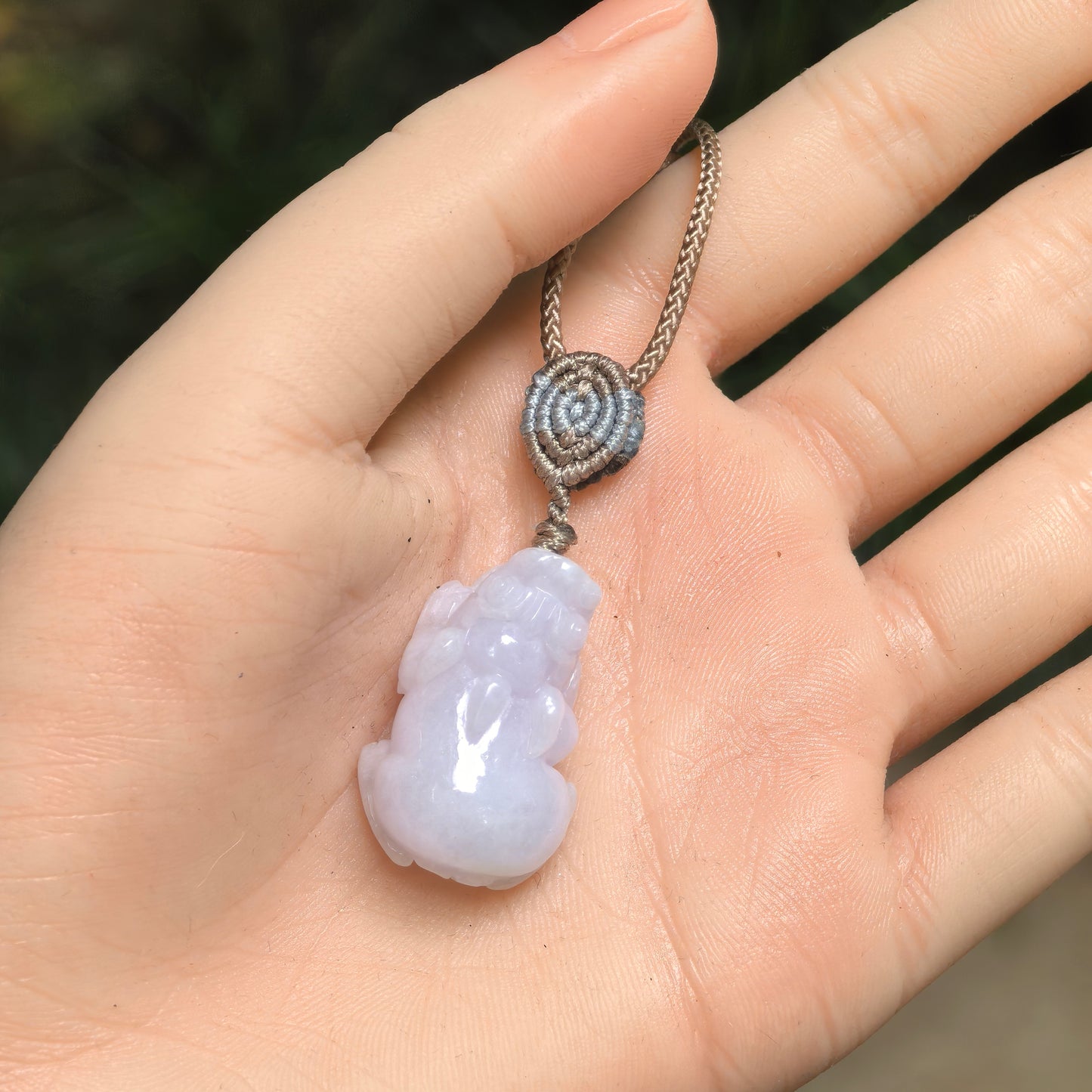 Handheld pale lavender Burmese jadeite Pixiu pendant showing its compact three-dimensional carving.