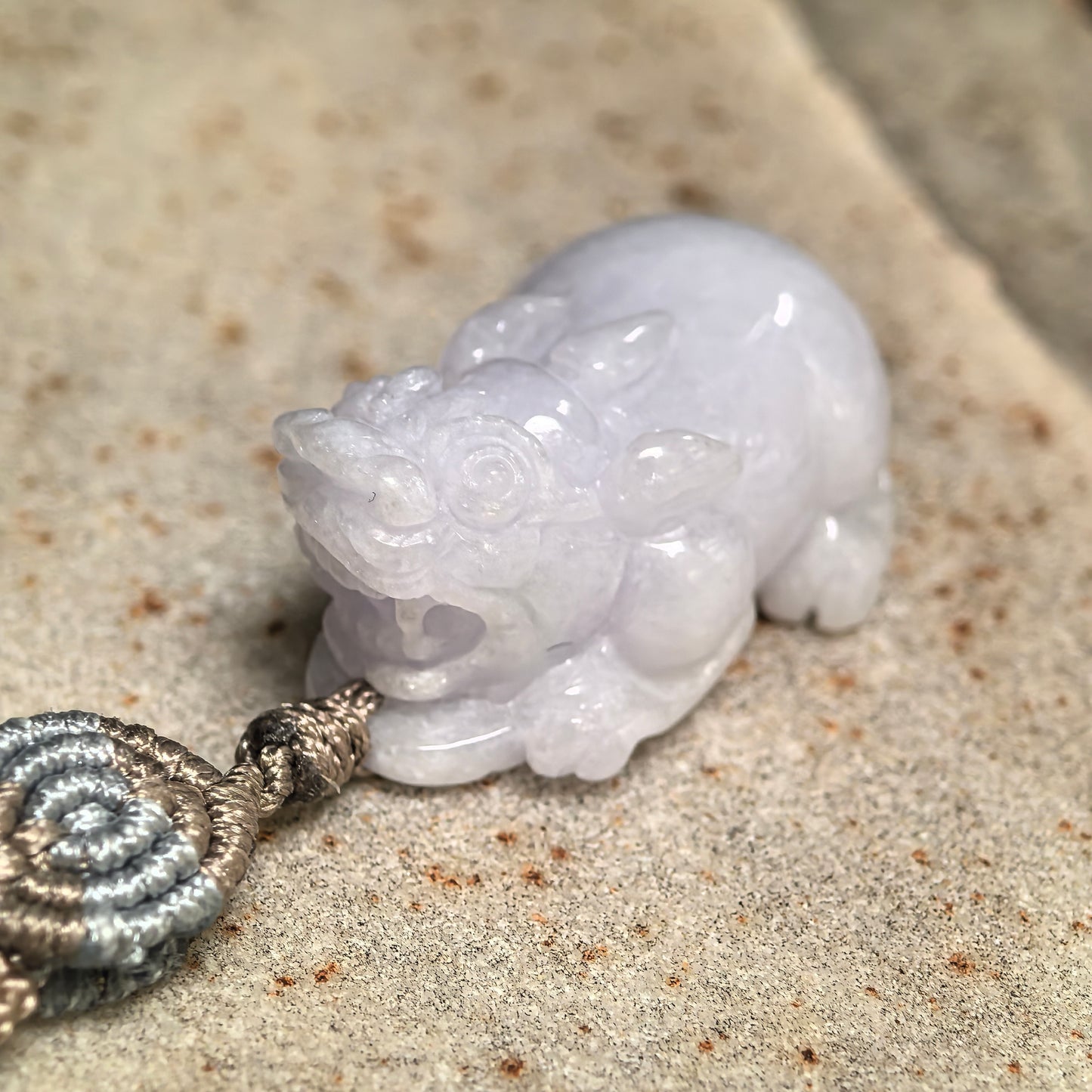 Close-up of the front of a glutinous pale lavender jadeite Pixiu pendant with detailed facial features.