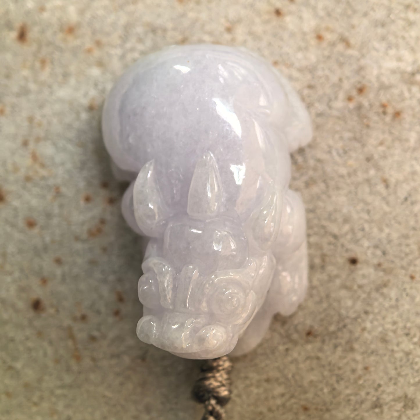 Side view of a pale lavender jadeite Pixiu pendant showing its substantial thickness and rounded contours.