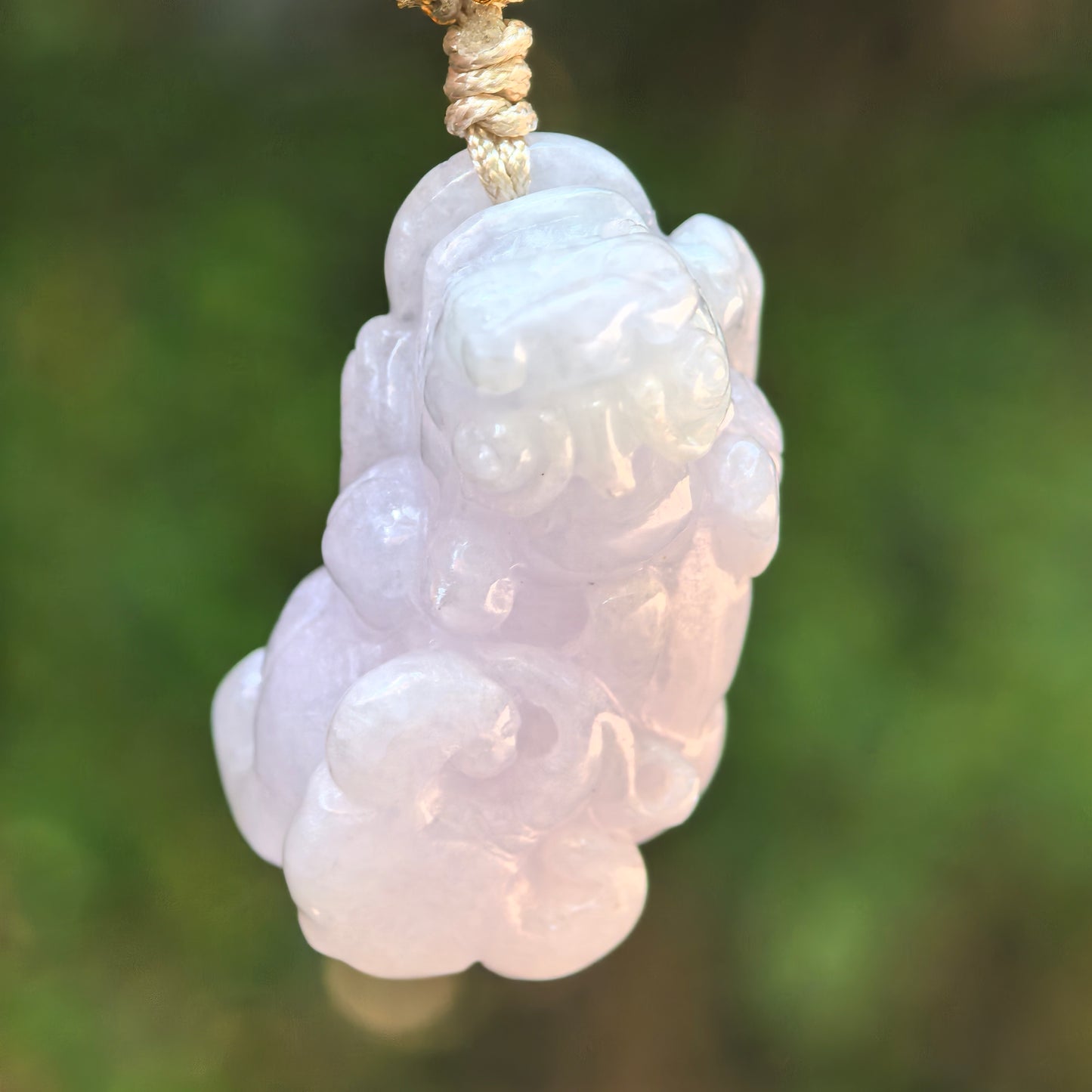 Natural Grade-A glutinous light spring Pixiu jadeite pendant hanging from a woven cord against a green background.