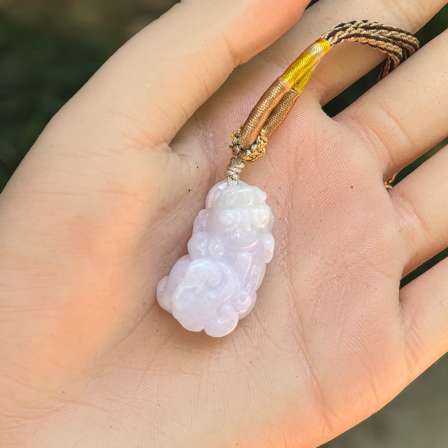 Hand-held pale lavender and light green Pixiu jadeite pendant showing its compact three-dimensional carving.