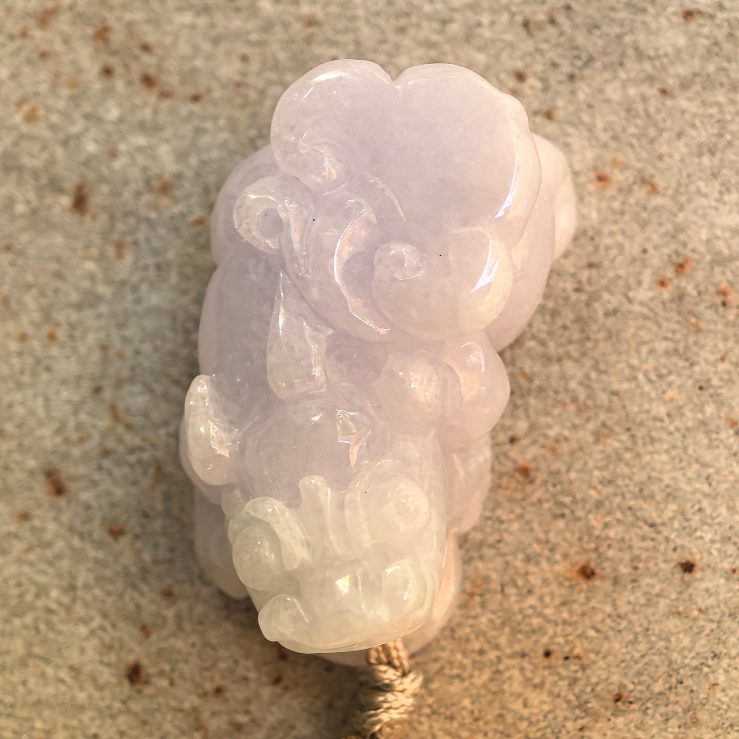 Top view of a glutinous pale lavender and light green Pixiu jadeite pendant showing its carved facial features and curled details.