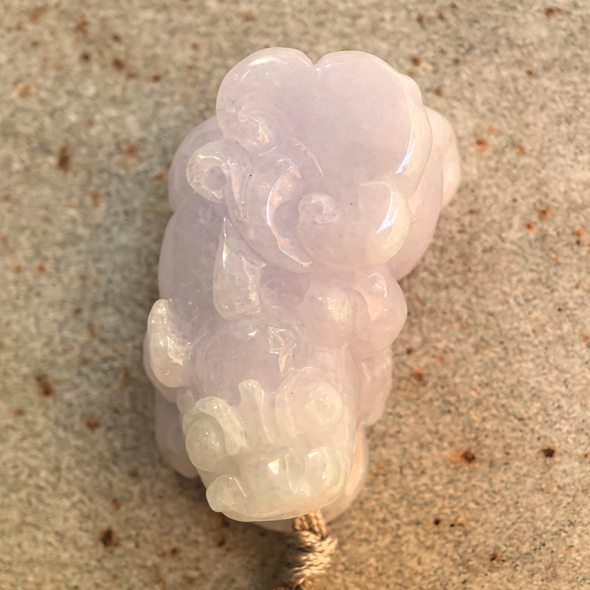 Top view of a glutinous pale lavender and light green Pixiu jadeite pendant showing its carved facial features and curled details.