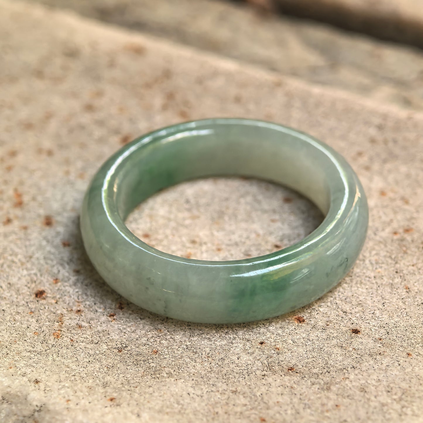 Close-up of an icy glutinous light green jadeite ring band resting on stone with natural green color variation.