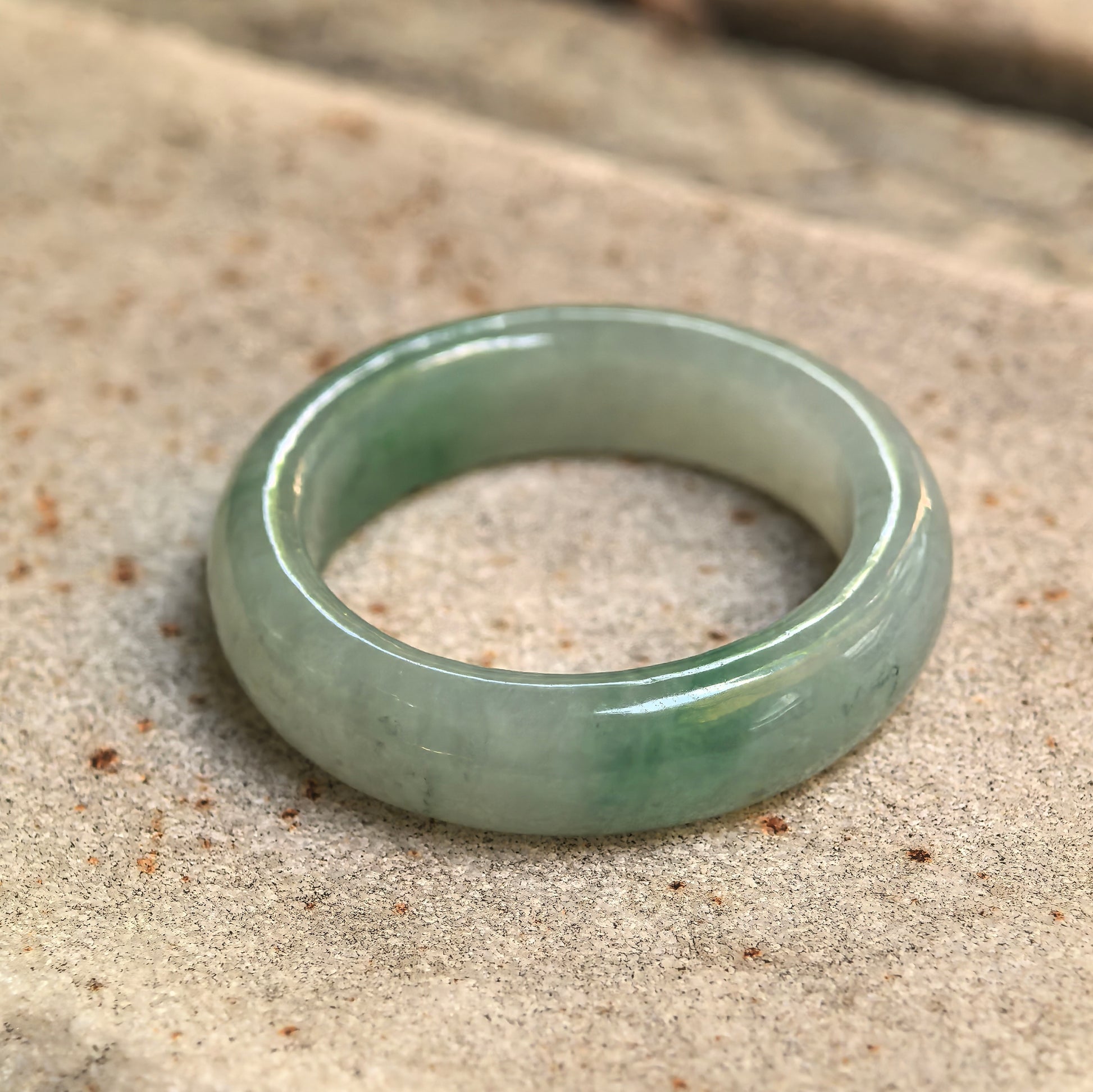 Close-up of an icy glutinous light green jadeite ring band resting on stone with natural green color variation.
