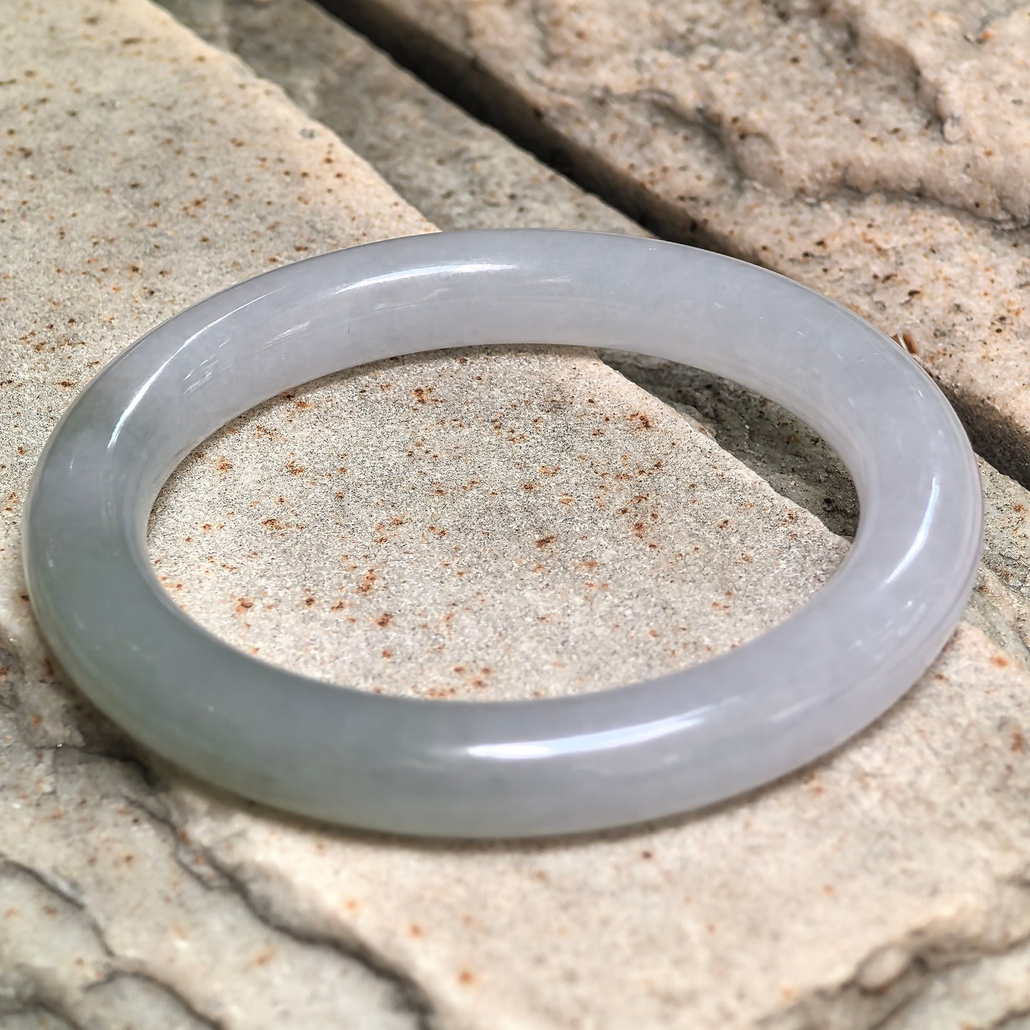 Natural Grade-A fine icy glutinous pale lavender and green round jadeite bangle showing its smooth polished surface.